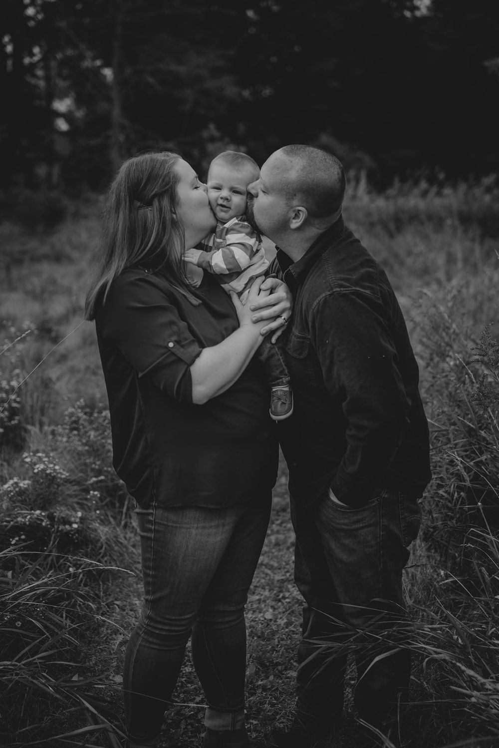 A family sharing an intimate moment with their baby in a black and white outdoor portrait.