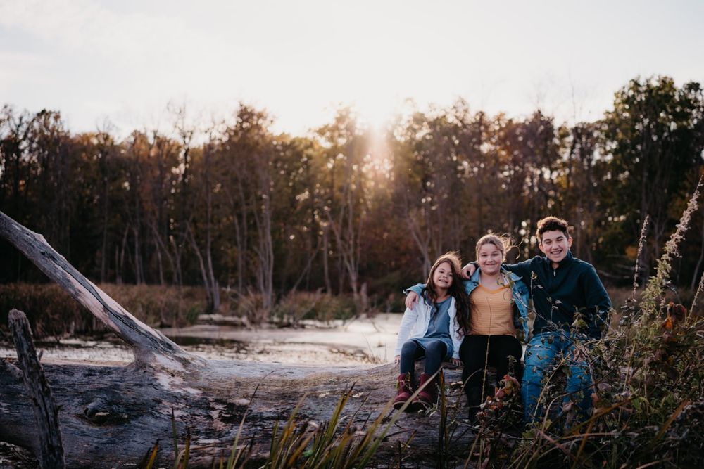 A family sitting together on a fallen log during sunset in a natural outdoor setting.