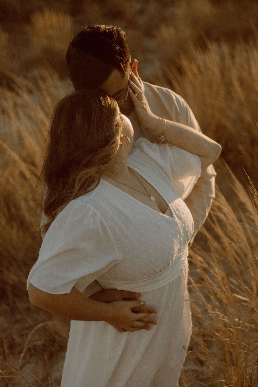 An intimate moment captured between two people in white clothing against golden beach grass.