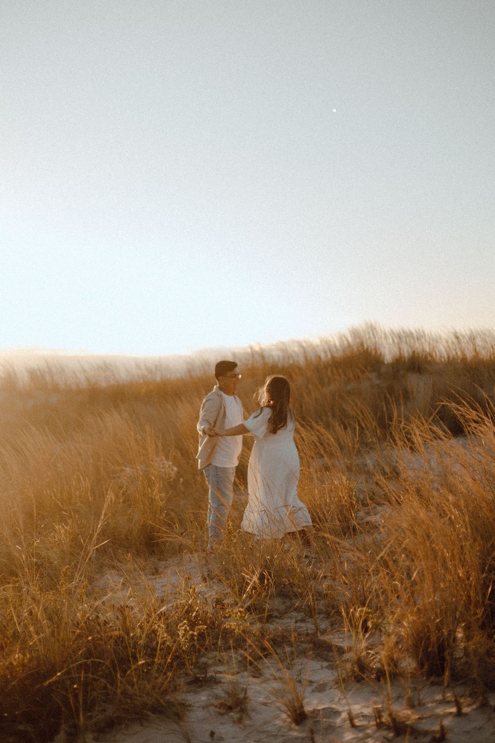 Two people walking through golden beach grass during a warm sunset.