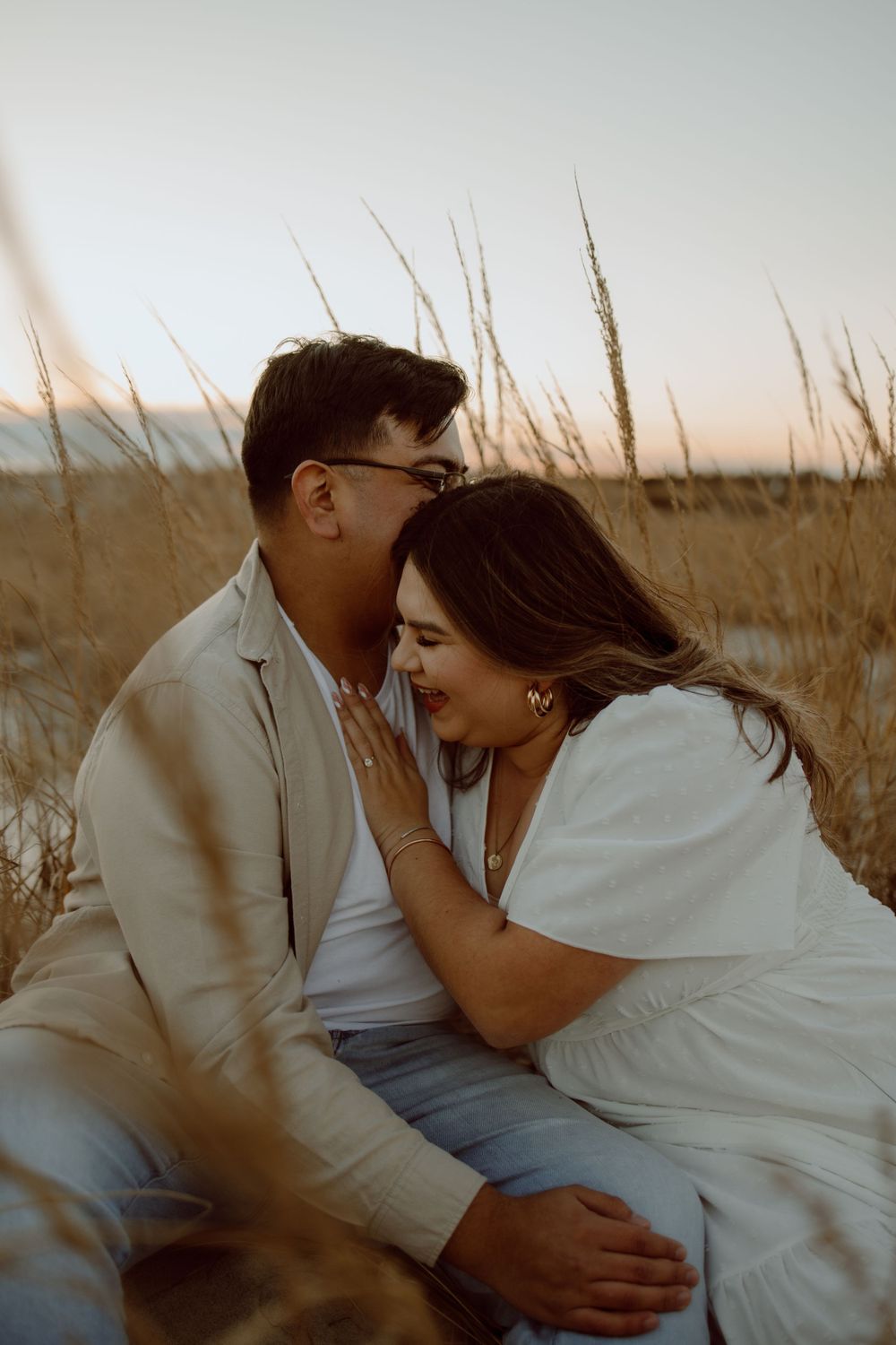 Loving couple shares intimate moment while sitting in coastal dunes.