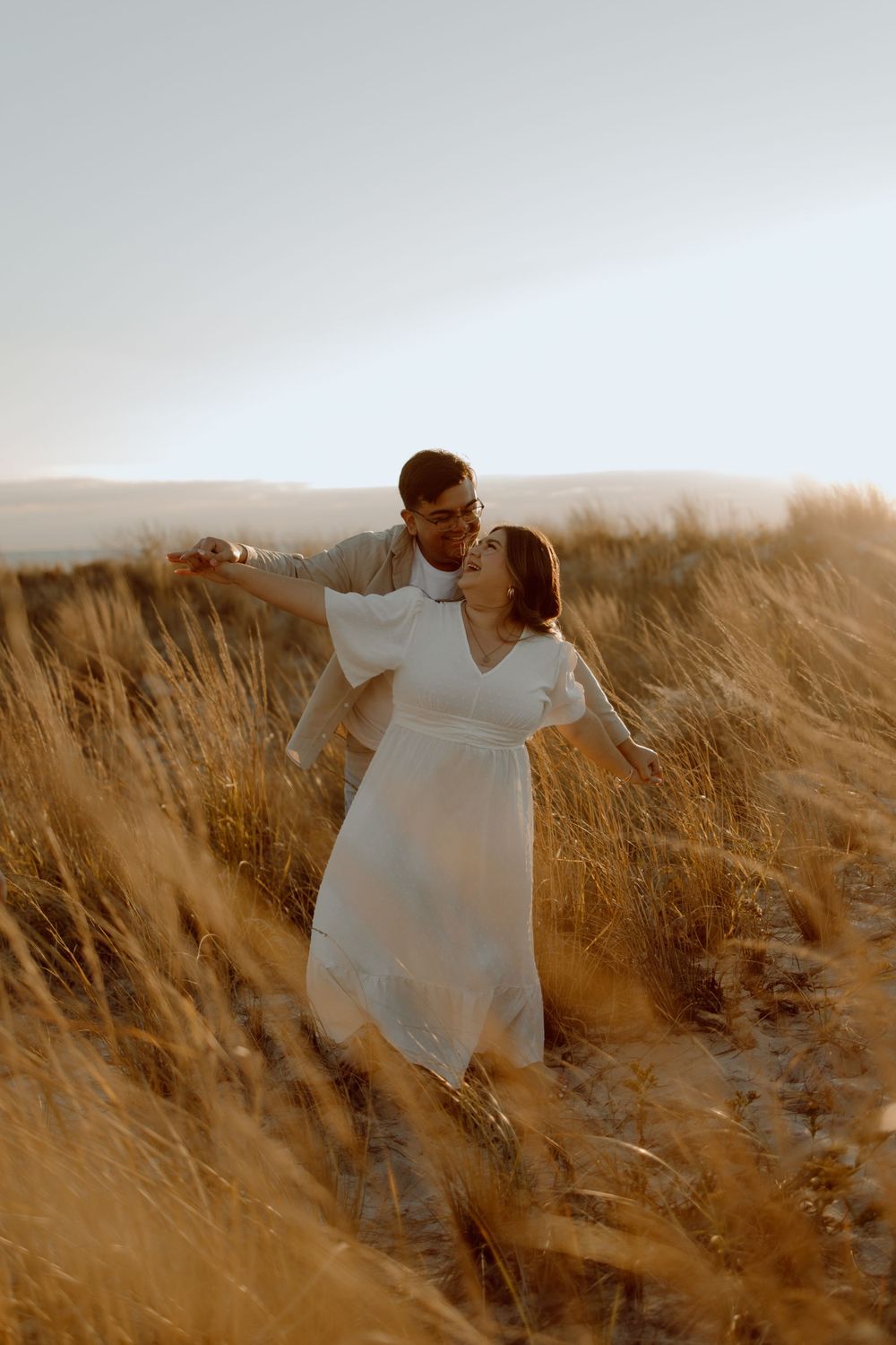 A romantic sunset moment in tall golden grass with flowing white dress and warm lighting.