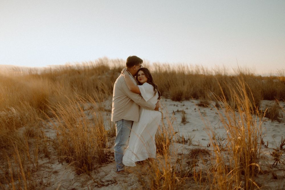 Couple shares tender moment among beach grass at golden hour.