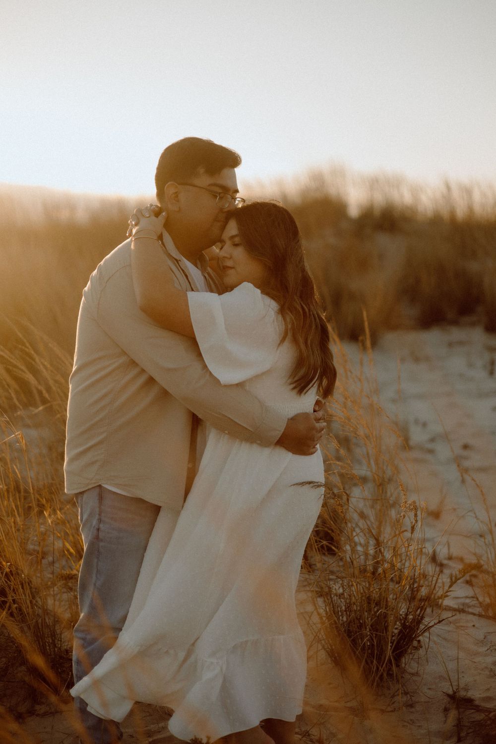 A couple sharing a romantic moment among coastal dunes at sunset.