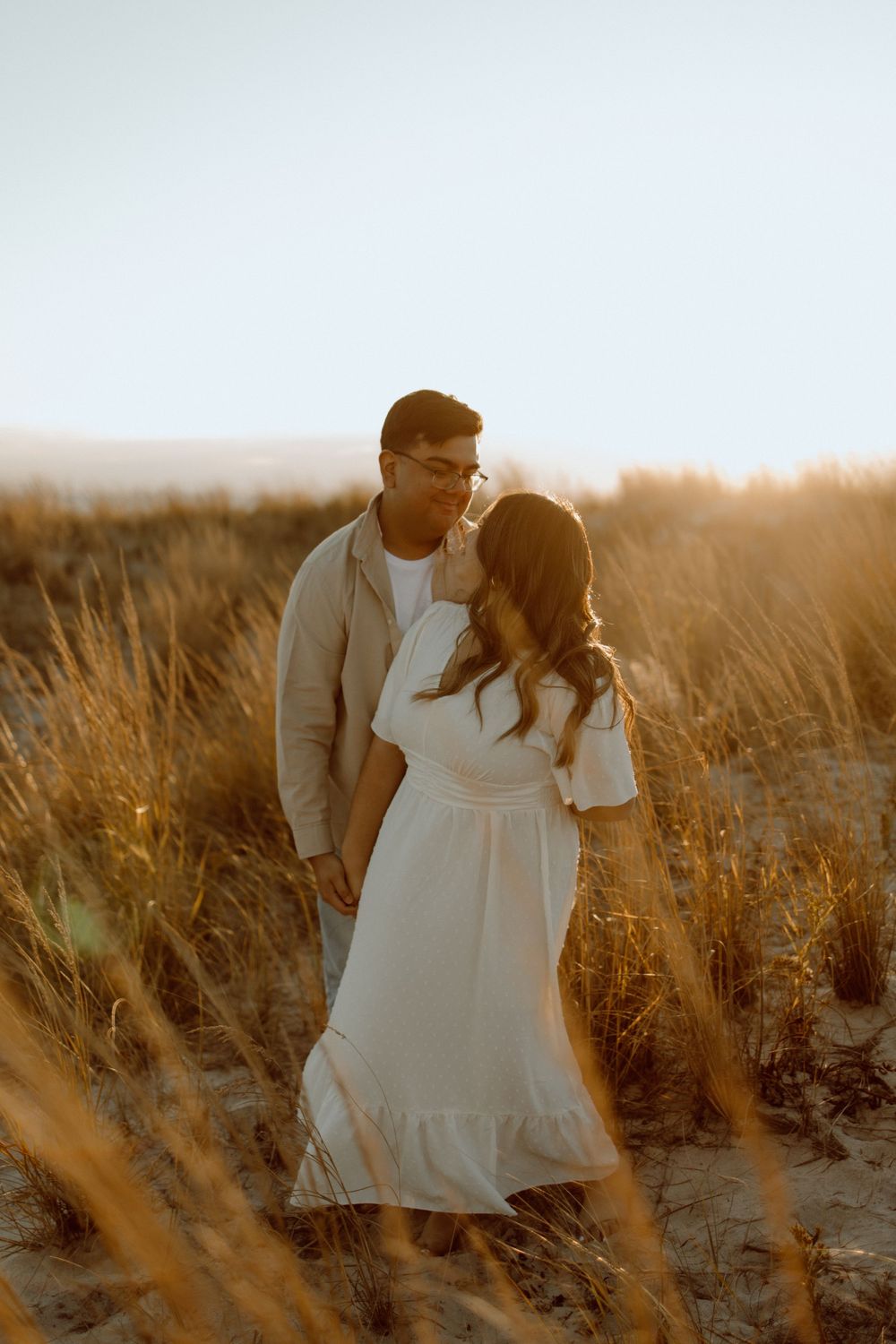 A romantic sunset portrait among windswept beach grass with warm golden lighting.