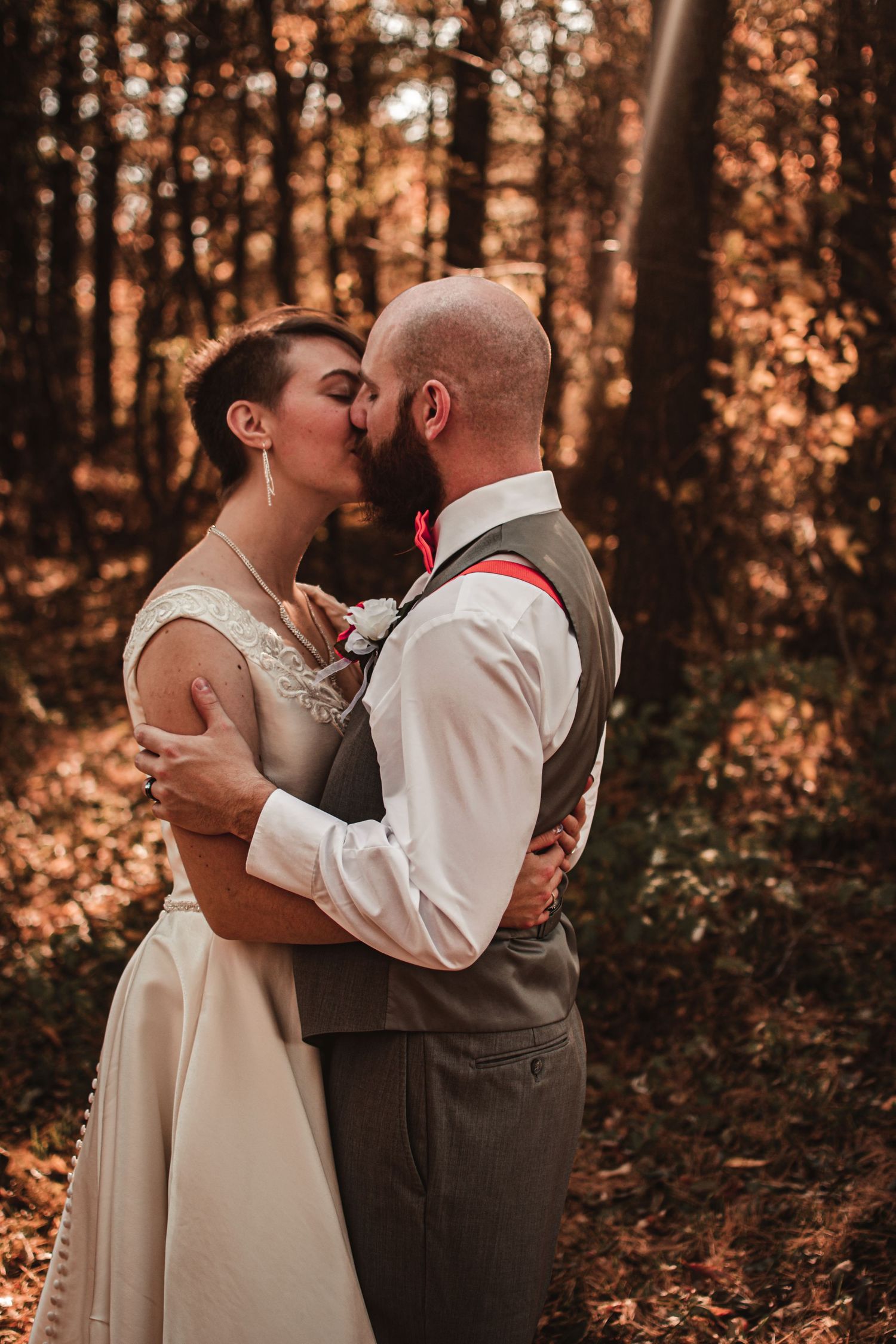 Romantic wedding couple embrace in autumn forest setting.