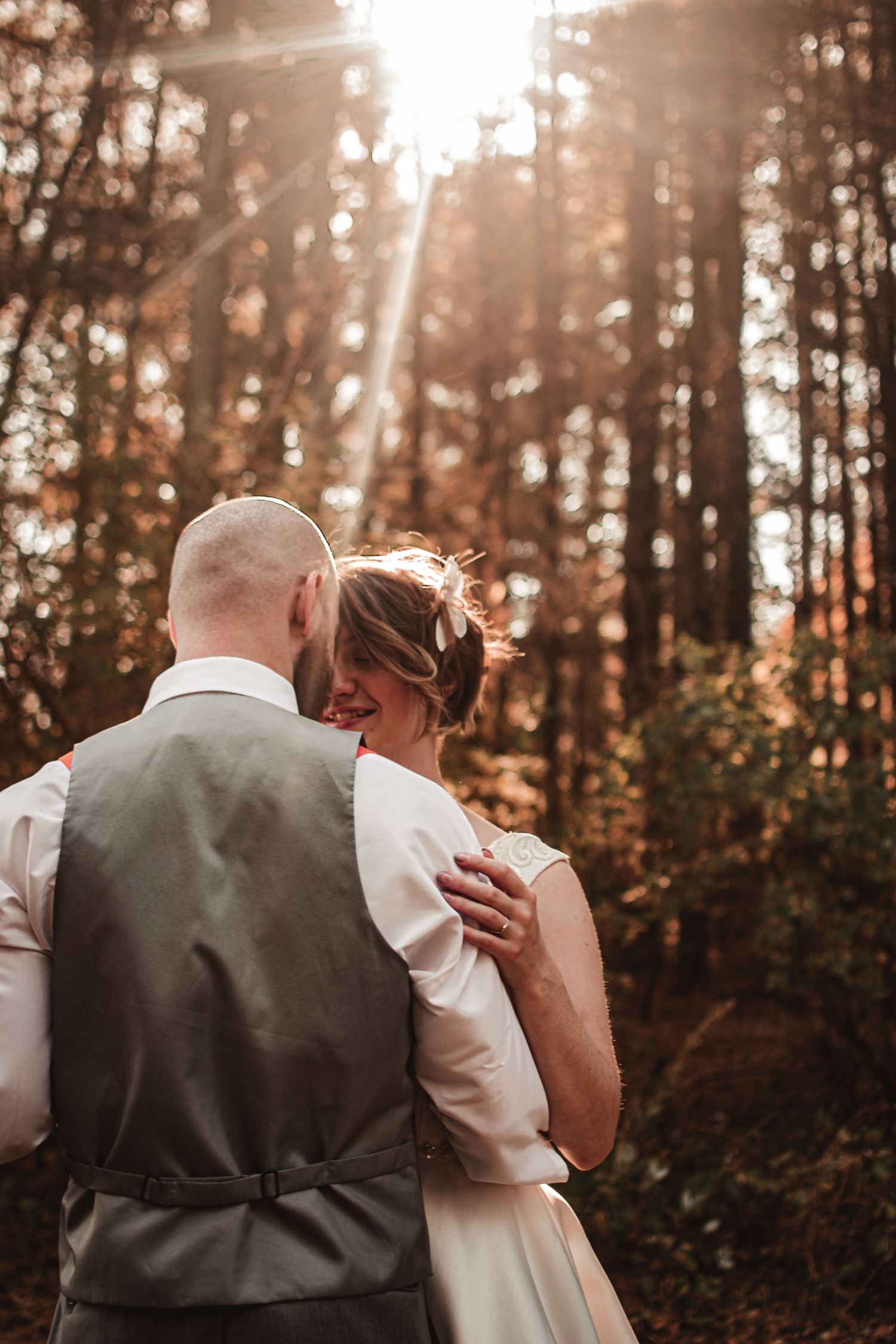 Newlyweds share intimate moment in sunlit autumn forest.