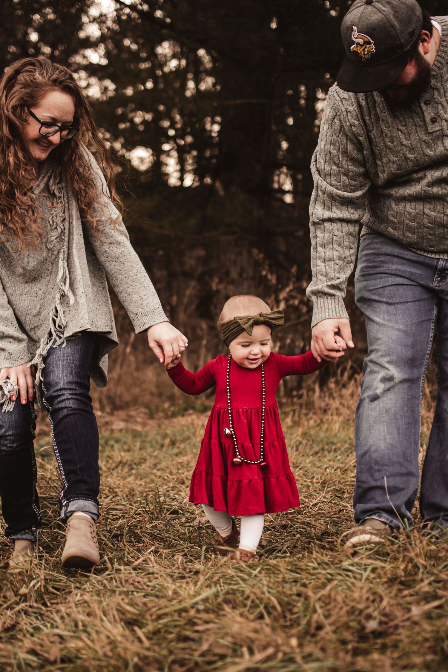 A child in a red dress holds hands while walking with others through a wooded area.