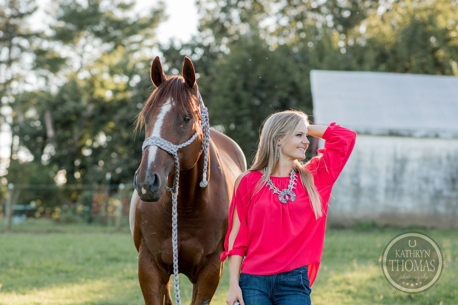 A chestnut horse stands calmly while its handler poses in a bright red sweater outdoors.