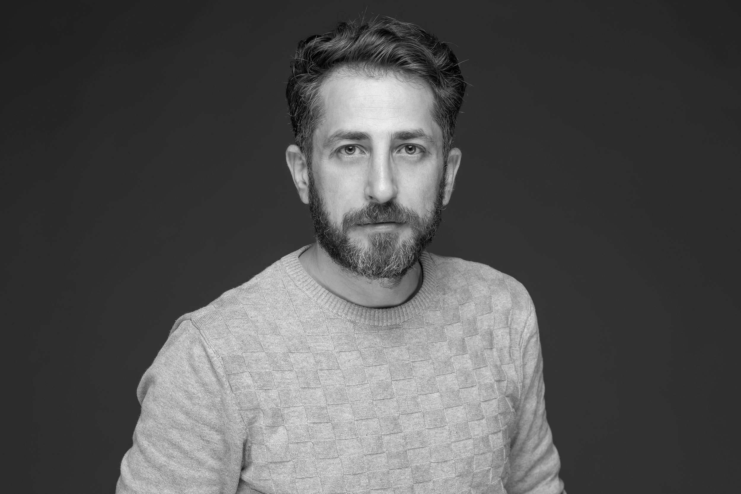 Professional studio portrait against dark background in monochrome style.