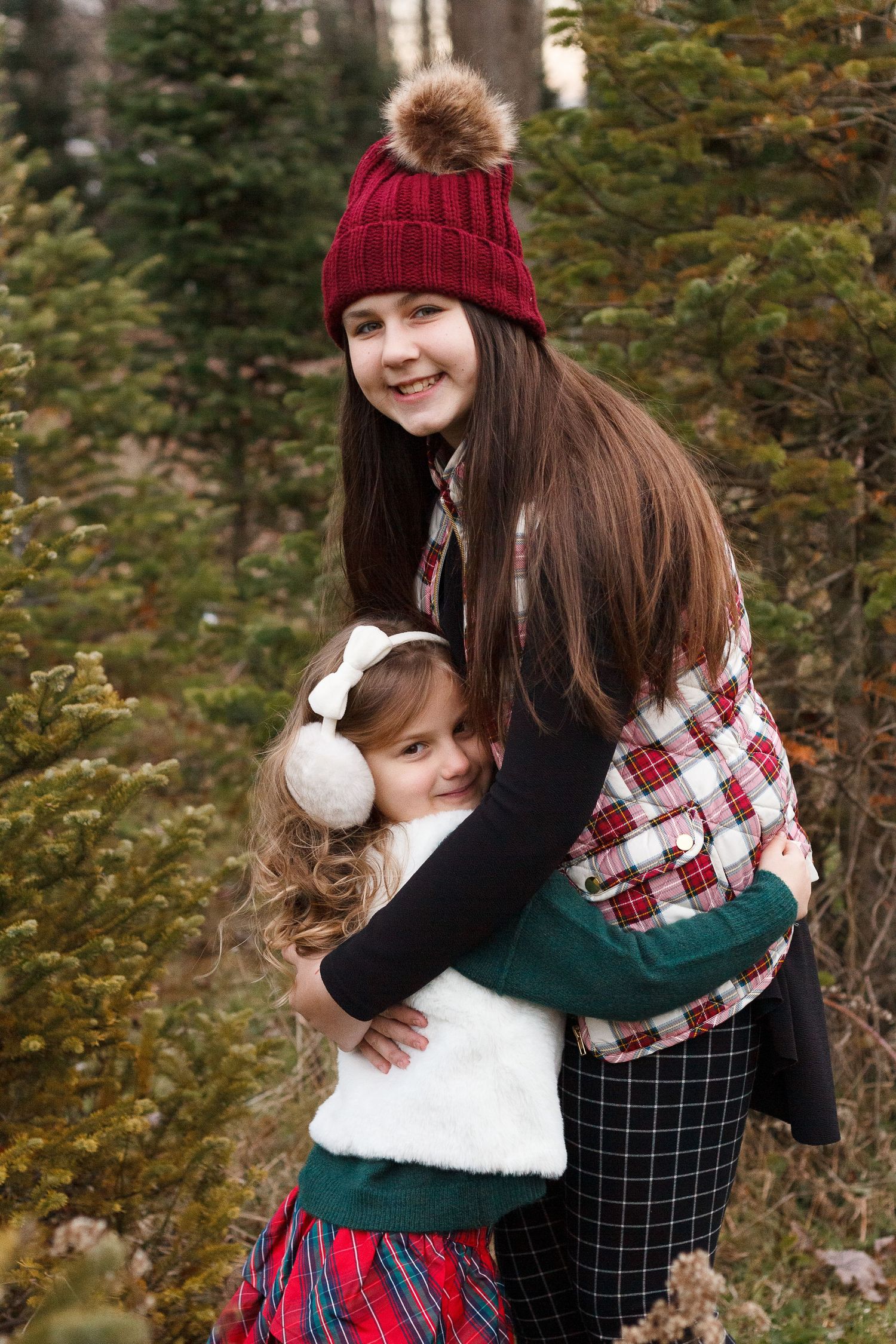 Winter portrait of two in festive holiday attire sharing warm embrace among evergreen trees.