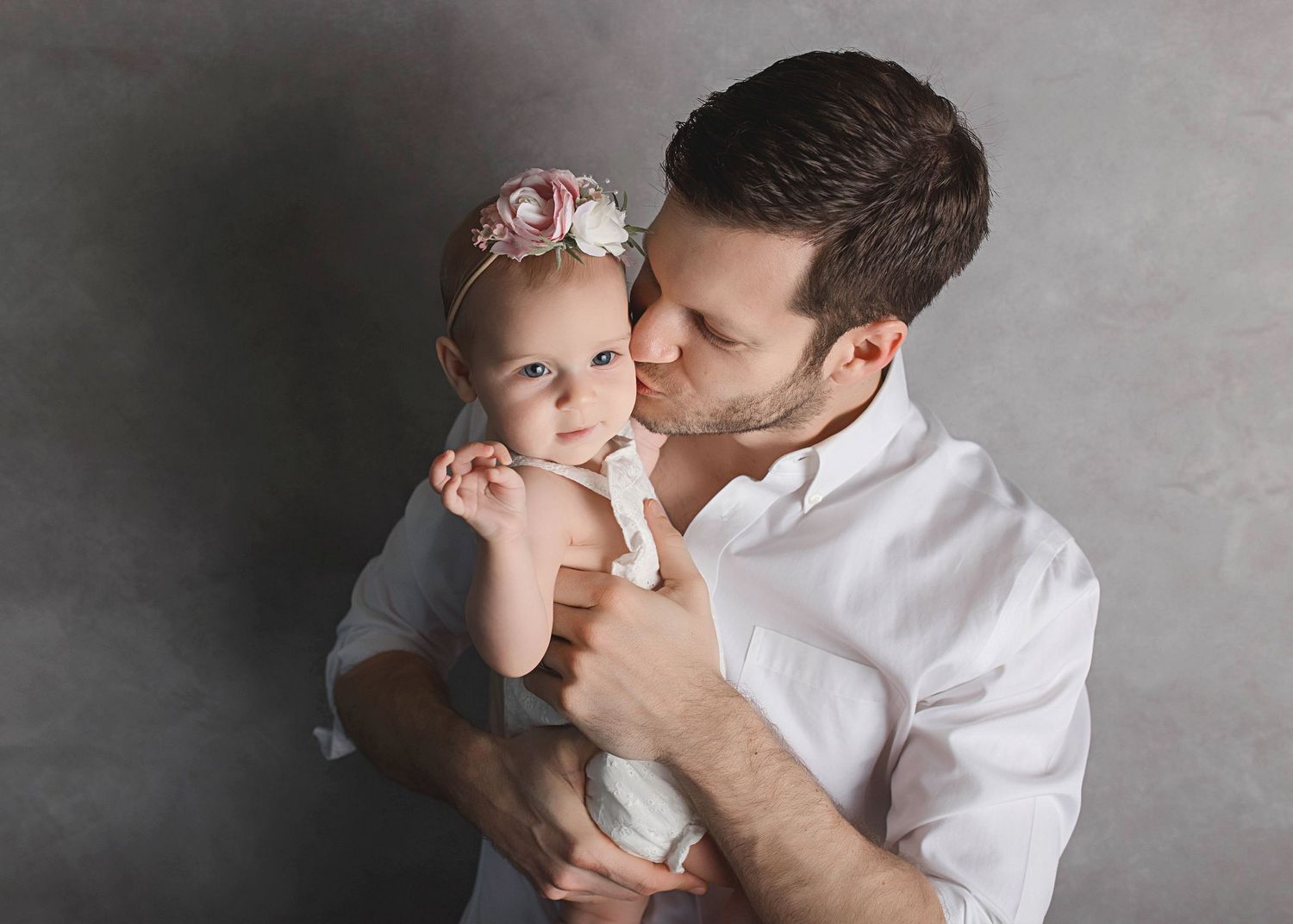 Intimate studio portrait in muted tones capturing tender moment against grey backdrop.