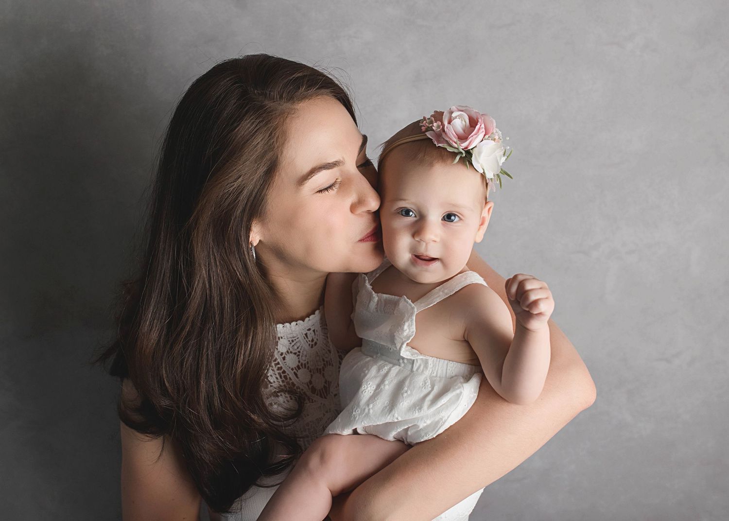 Sweet moment captured in studio against grey background with delicate floral accessories.