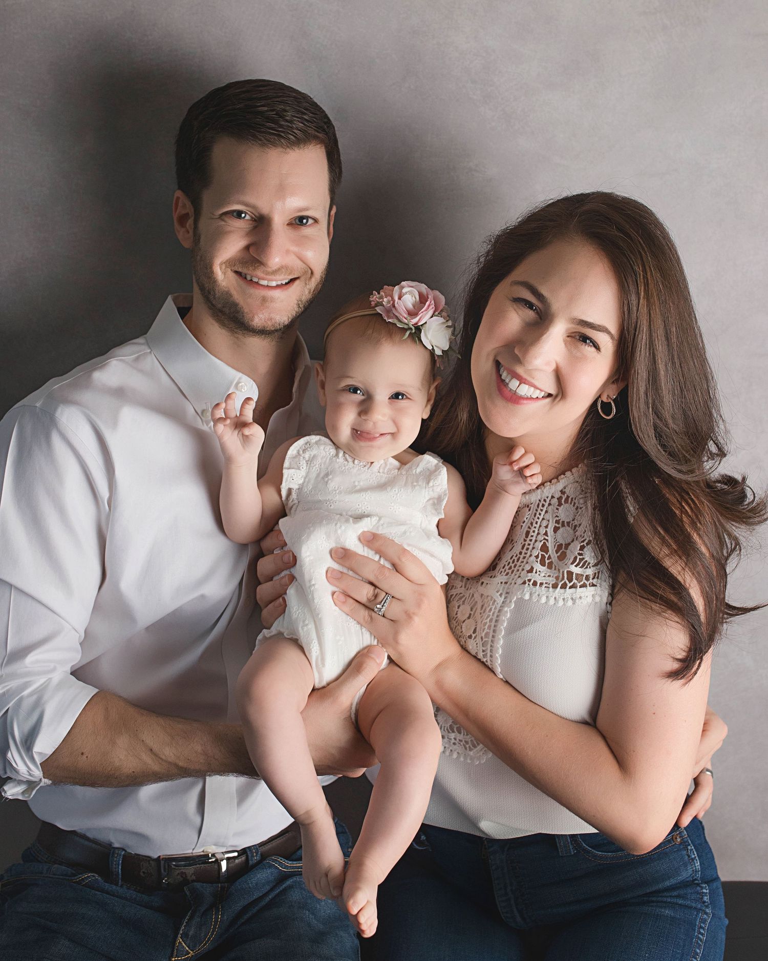Studio family portrait in coordinated white outfits against grey background.
