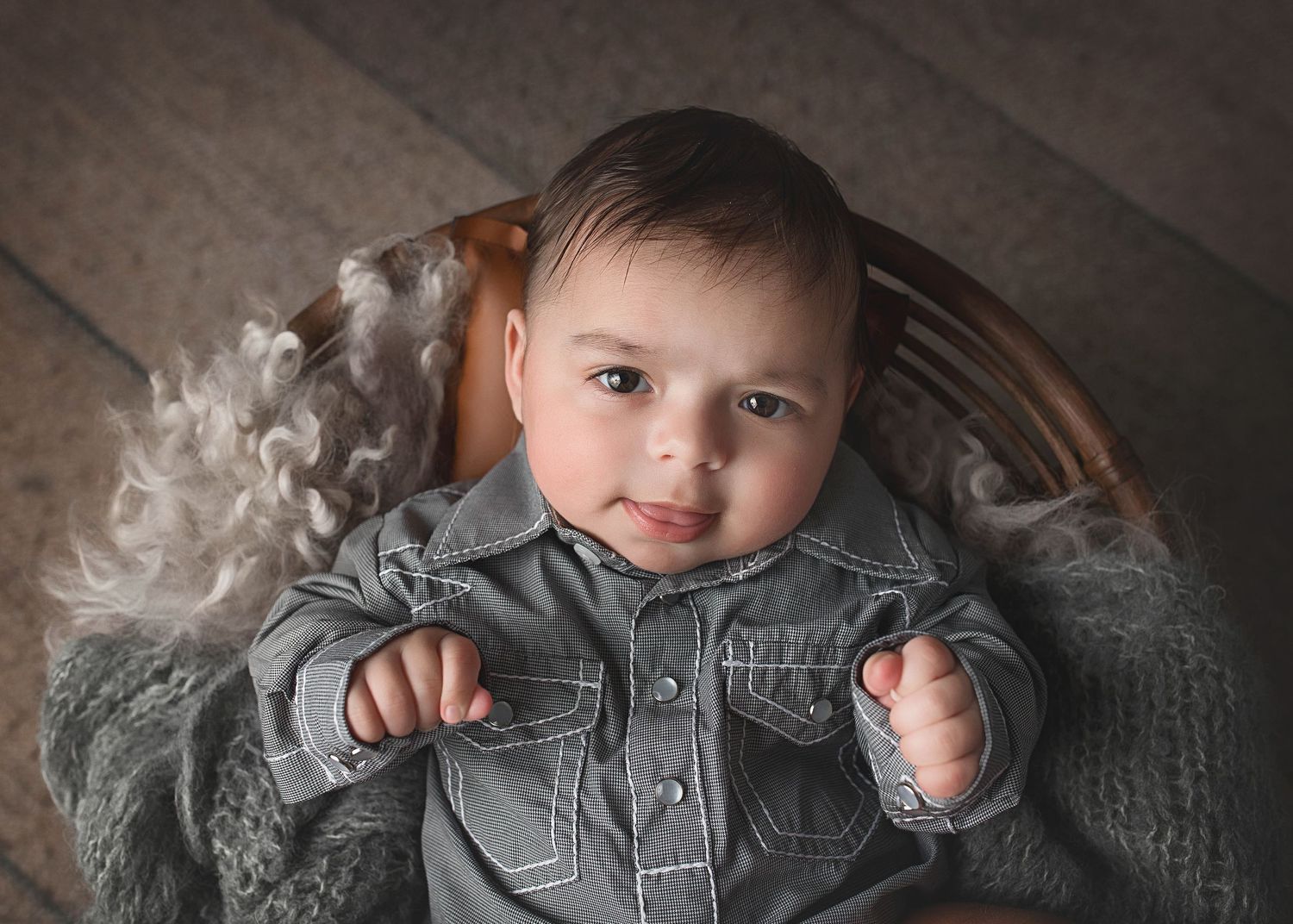 Baby in grey button-up outfit smiles while sitting in vintage chair with misty background effect.