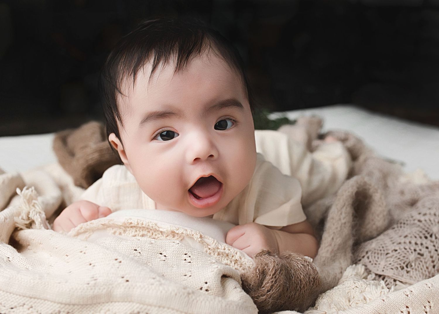 Infant with bright expression lying on delicate lace blanket in soft lighting.