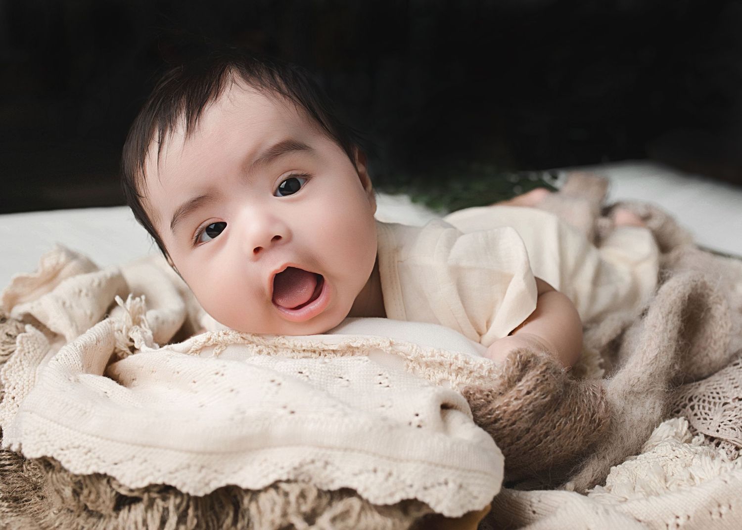 Baby lying on cream textured fabric with natural lighting in lifestyle portrait.