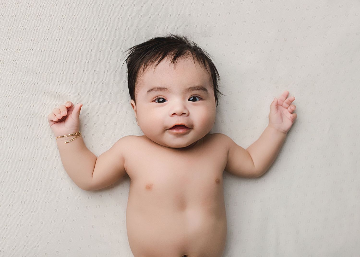 Baby with raised arms lying on simple cream background in natural portrait style.