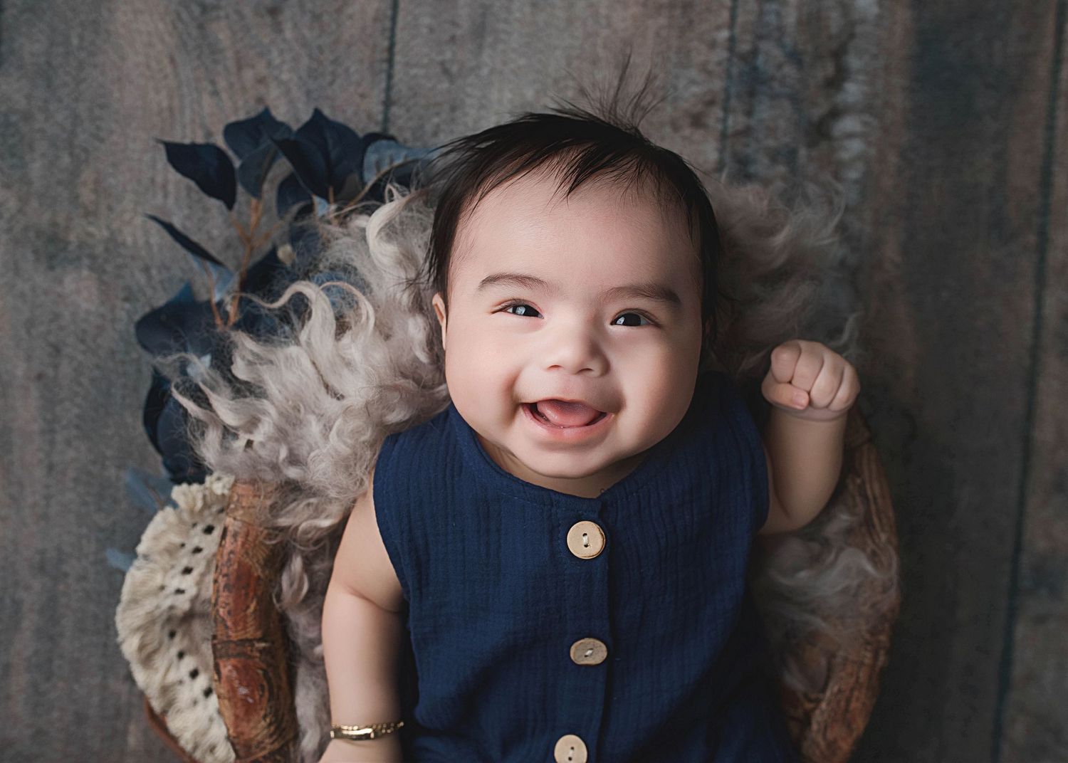 Smiling baby in navy button-up outfit against textured vintage background.
