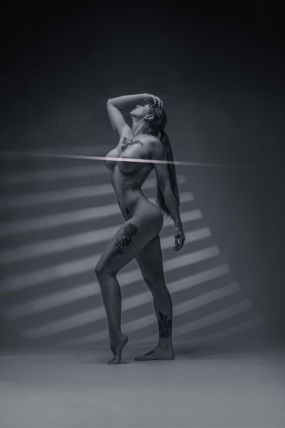 Monochrome studio portrait with striking light patterns across figure in dance pose.
