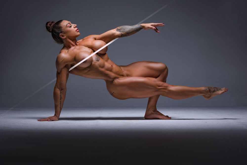 Athletic nude figure demonstrates graceful dance pose against dark background.