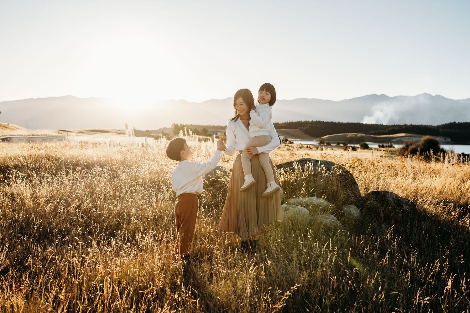A family stands in a golden field at sunset with mountains in the background.