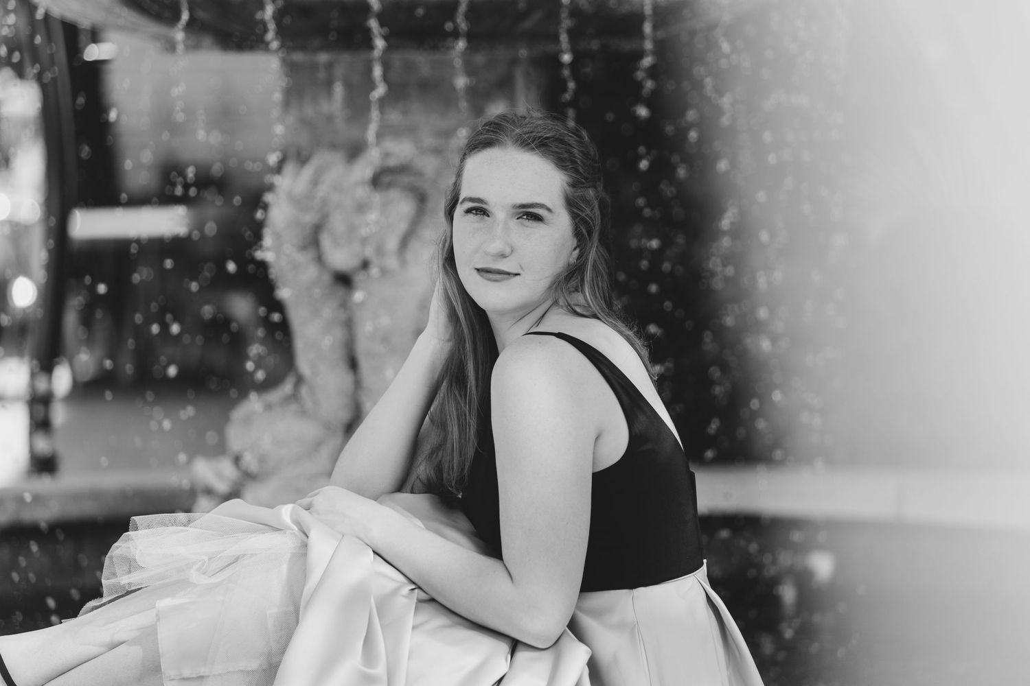 Black and white portrait of young woman in formal dress against sparkling backdrop.