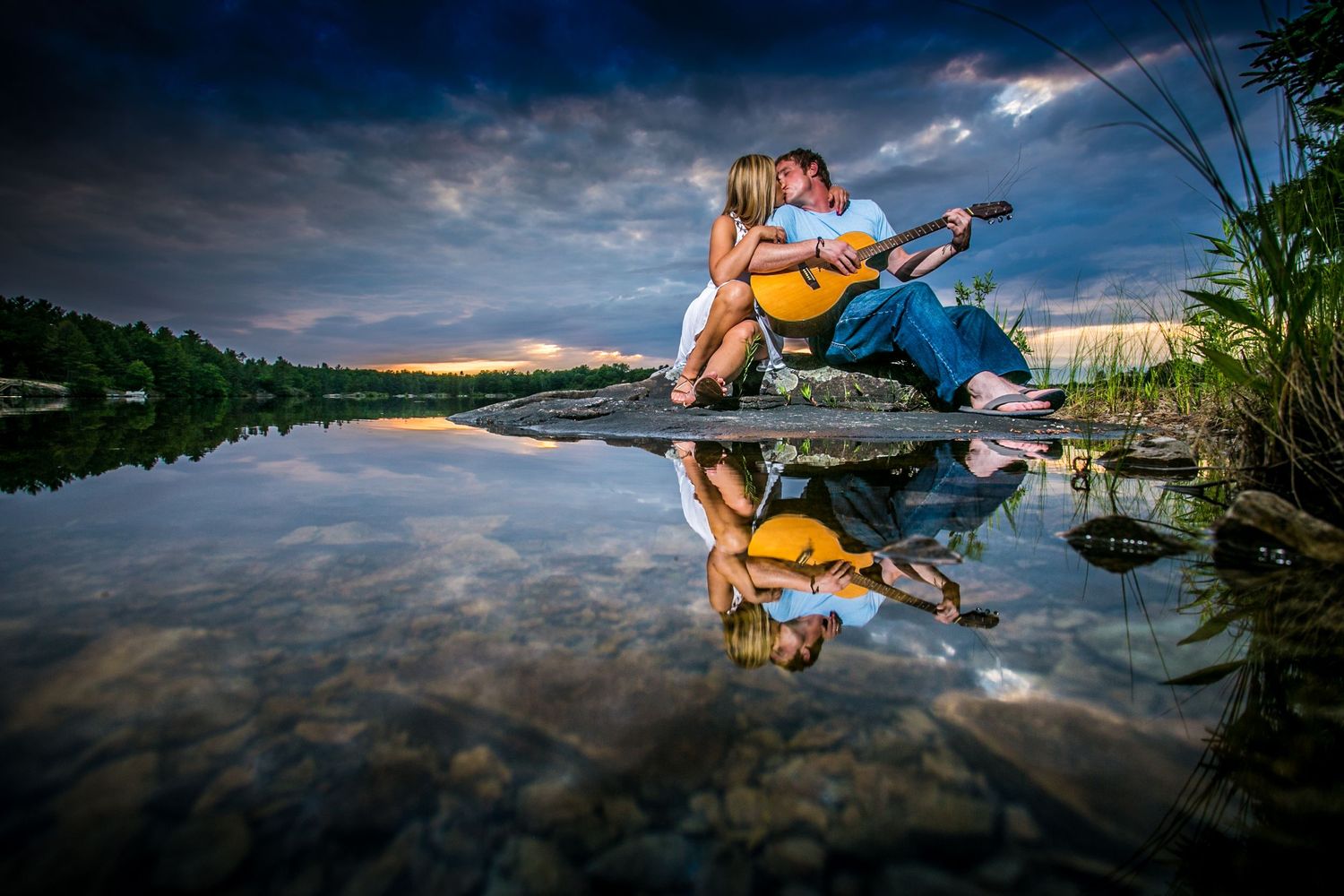 Romantic lakeside engagement photos with dramatic cloudy sky reflections.