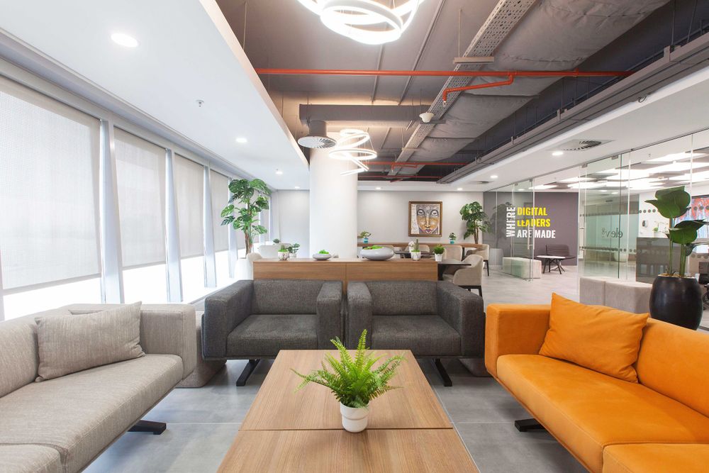 Open concept office area featuring orange sofa, minimalist decor, and industrial ceiling design.