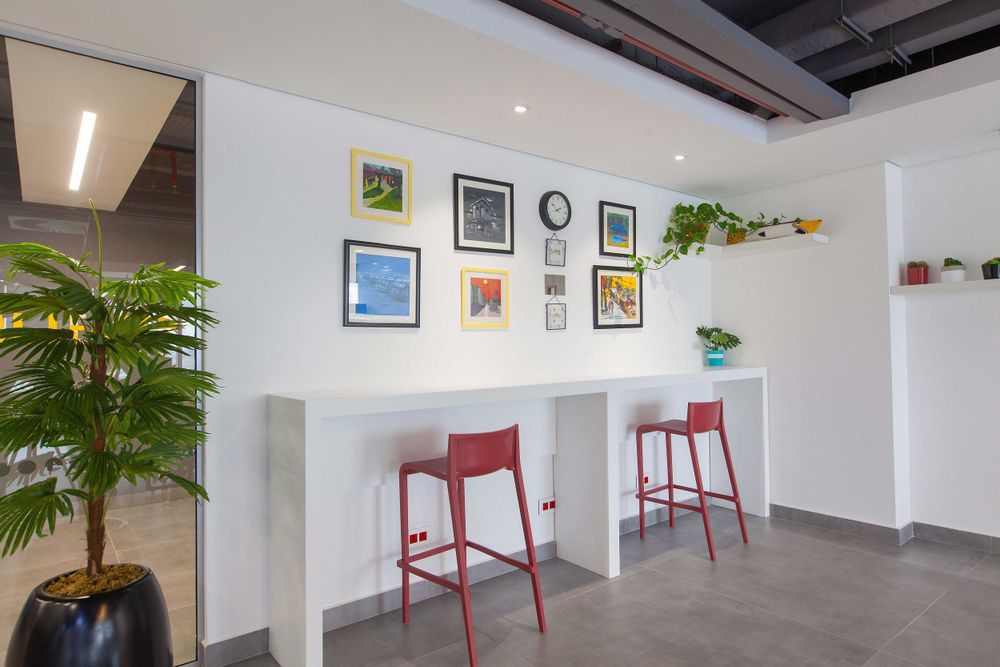 Clean white office space with minimalist decor, framed artwork, and indoor plants along the walls.
