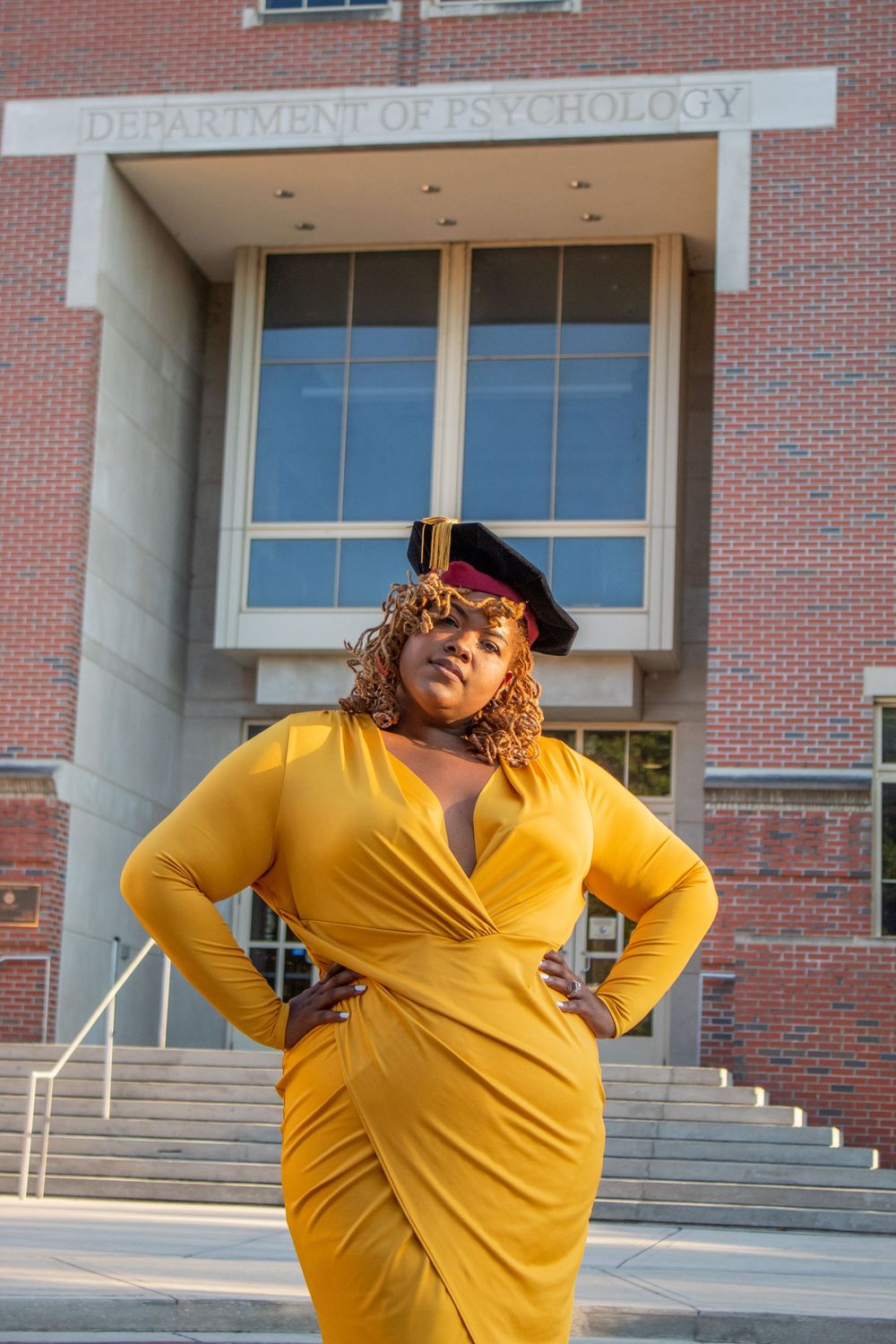 Professional portrait in front of psychology department building wearing yellow graduation attire.