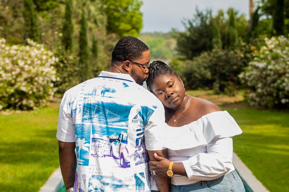Couple sharing intimate moment in blooming spring garden wearing white and printed outfits.