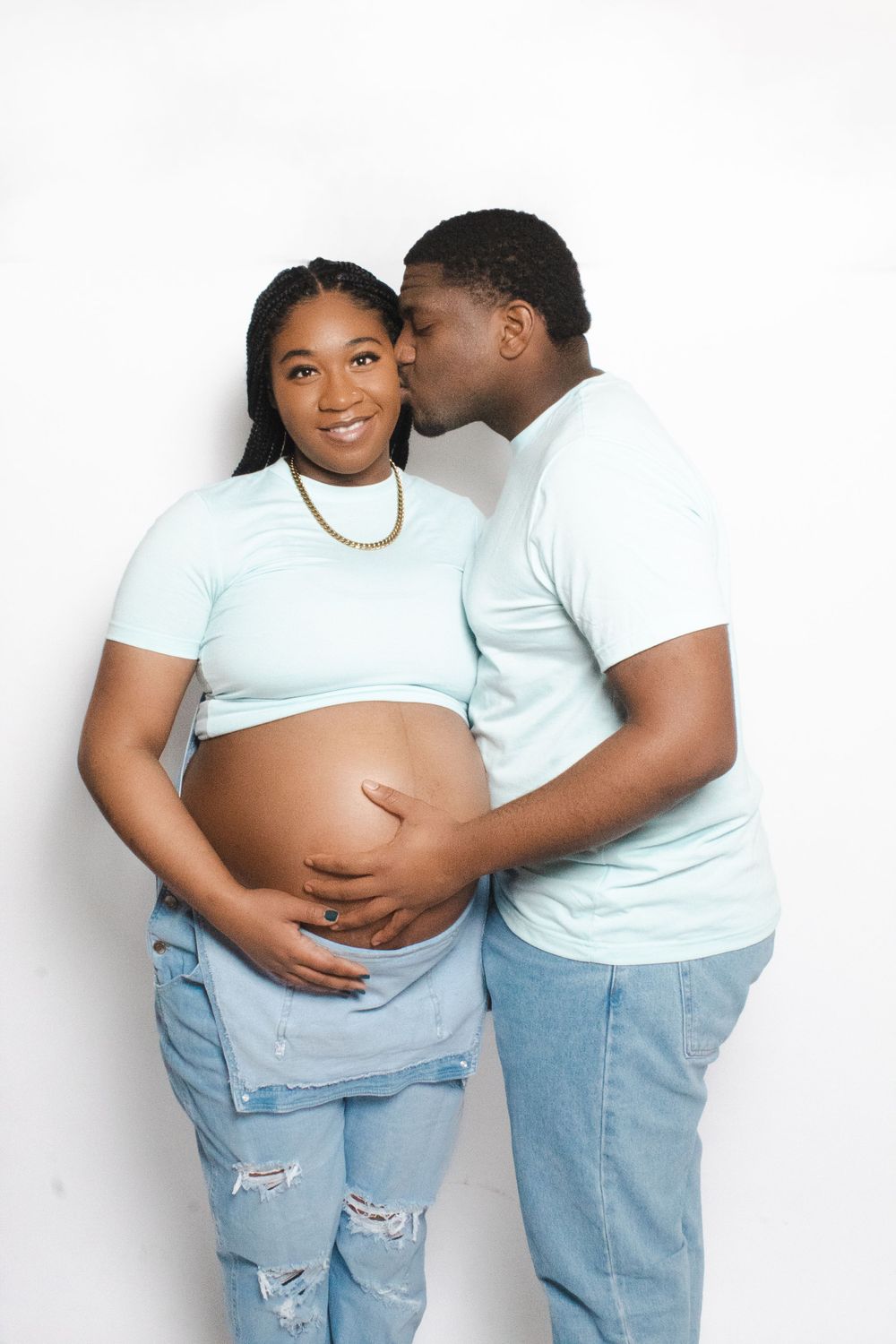 Maternity photoshoot with couple in matching light blue outfits and ripped jeans.