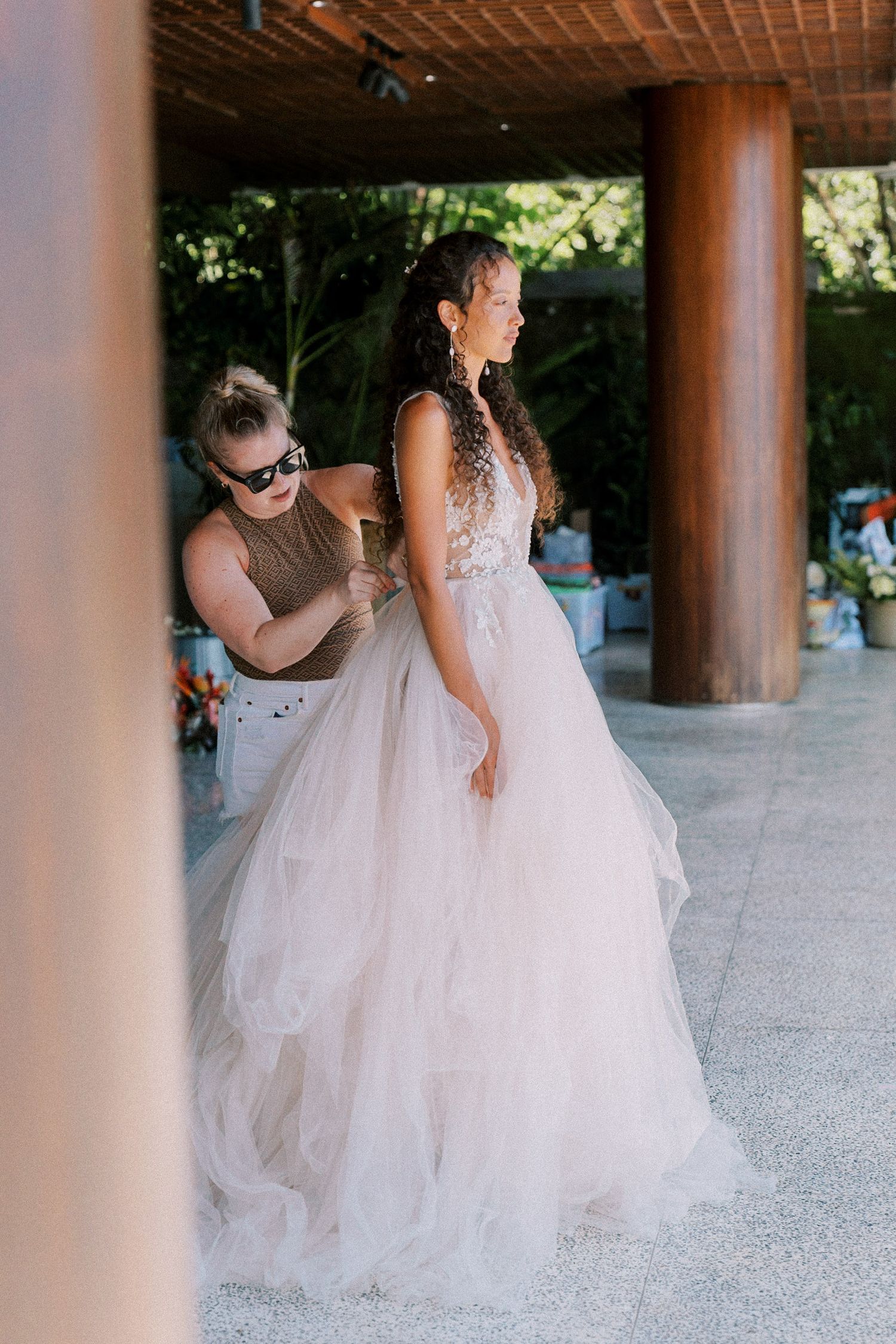 Wedding dress preparation moment under wooden colonnade with tulle skirt details.