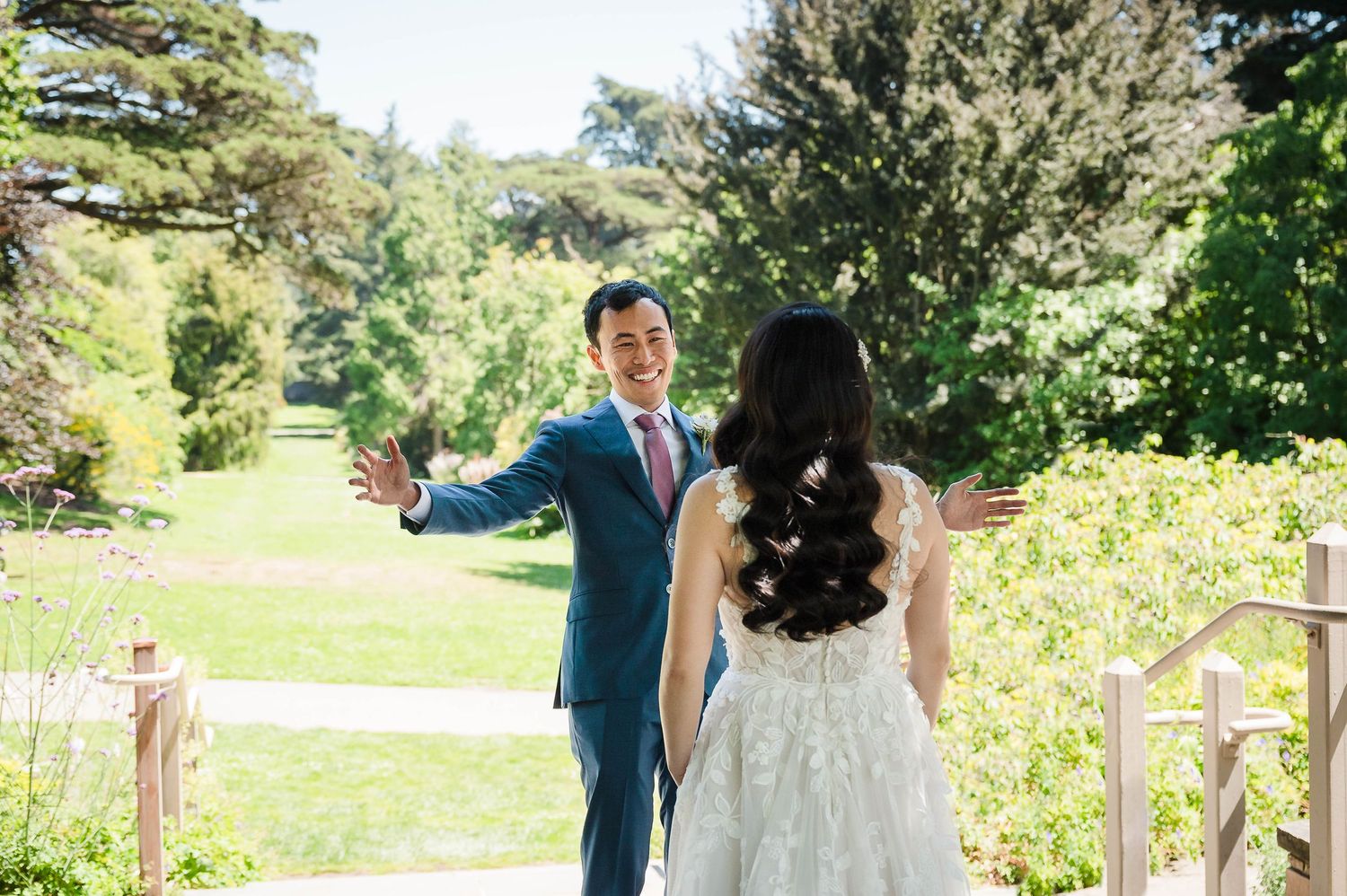 A newly married couple shares a joyful moment in a lush garden setting wearing formal wedding attire.