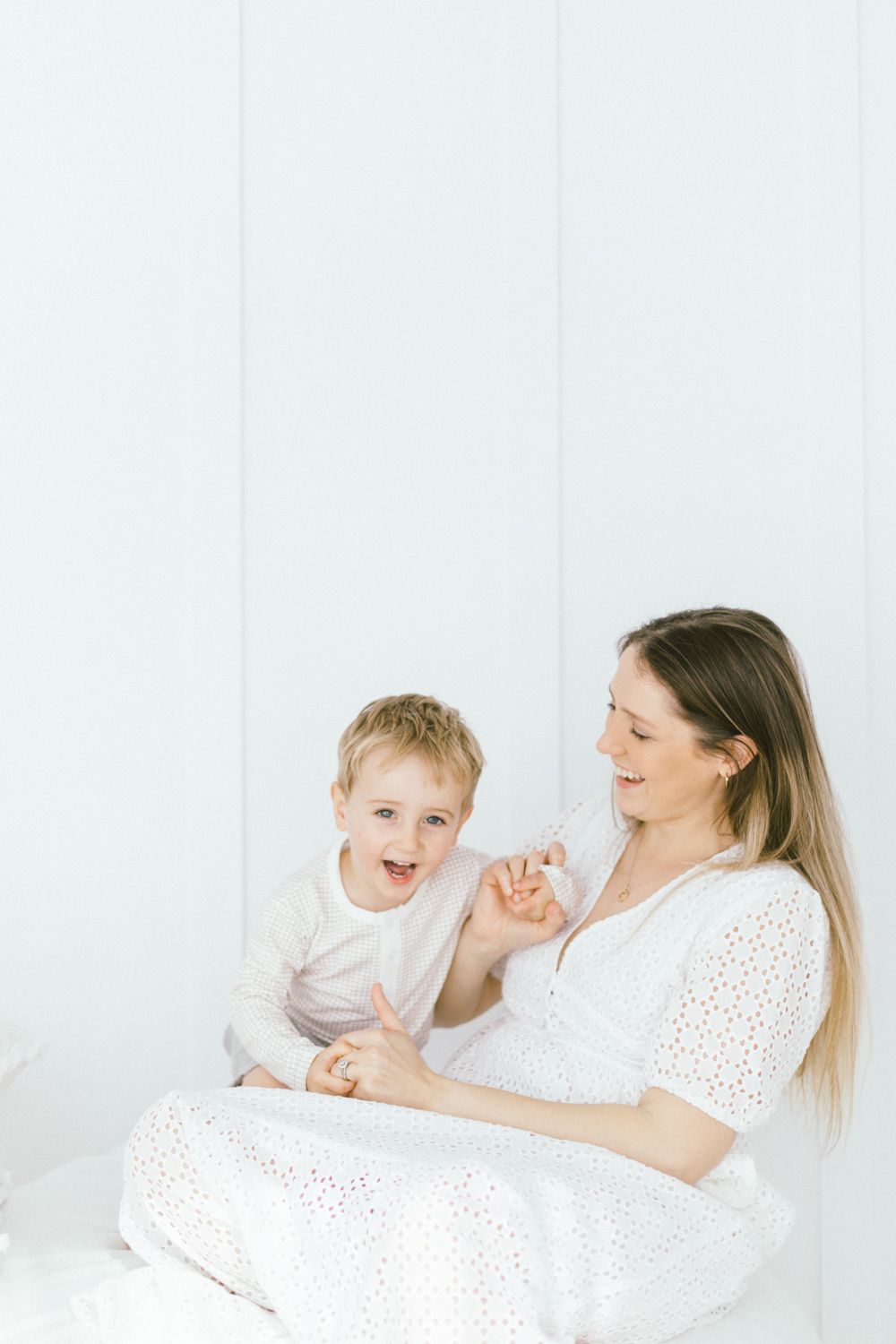 Parent and child share playful interaction on white bedding.