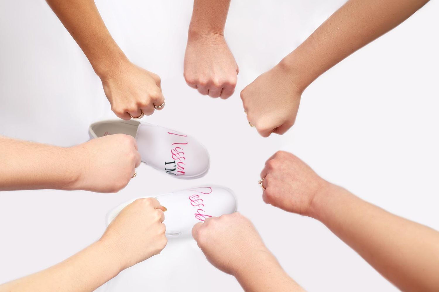 Multiple hands coming together in a circle holding pink socks against white background.