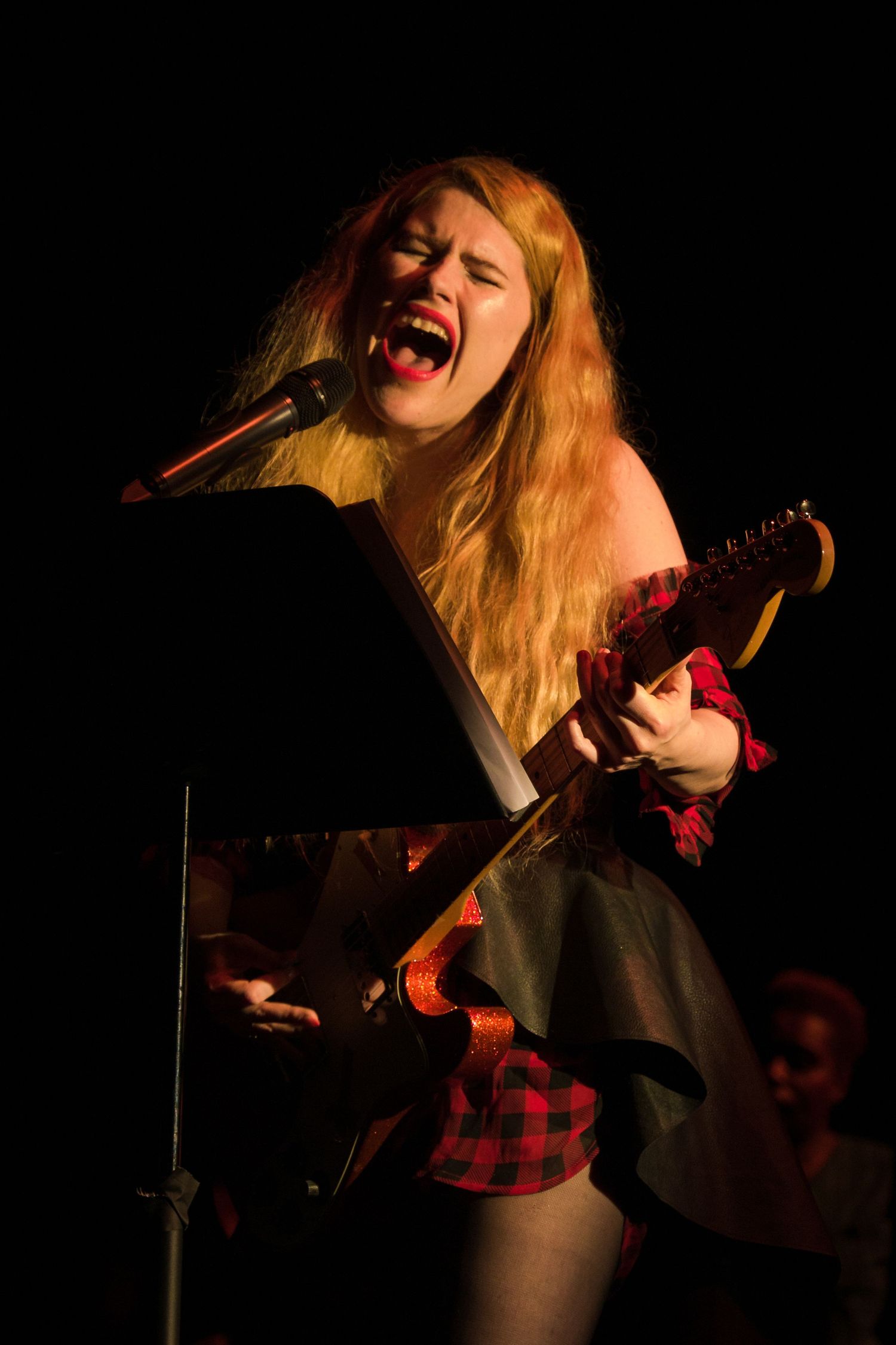 A performer passionately singing and playing guitar under dramatic stage lighting.