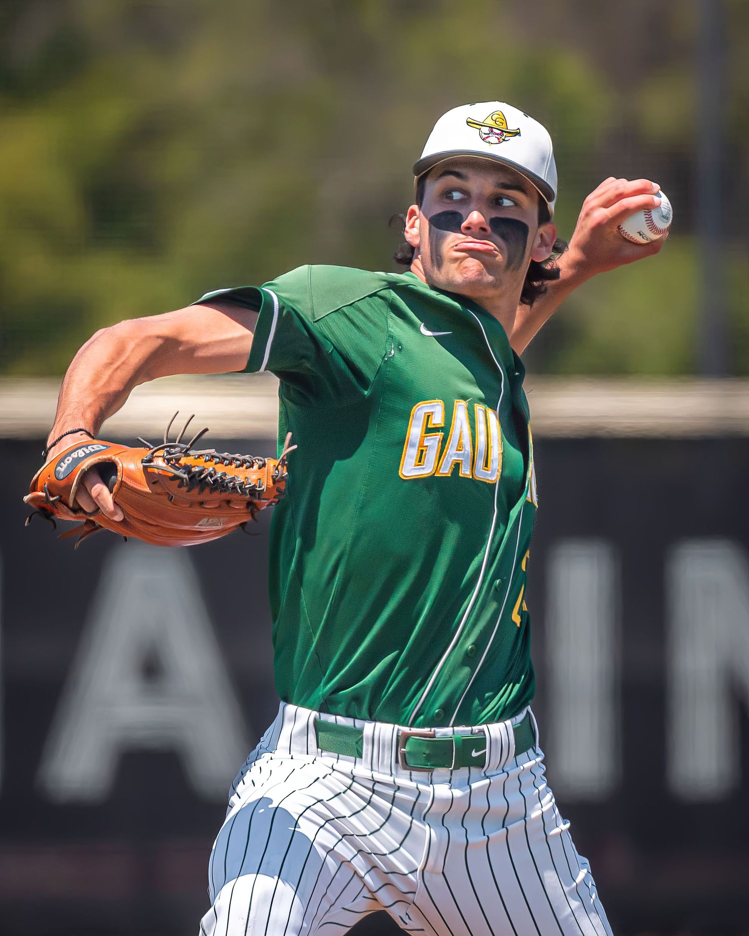 Baseball pitcher in green uniform winds up to throw during game action.