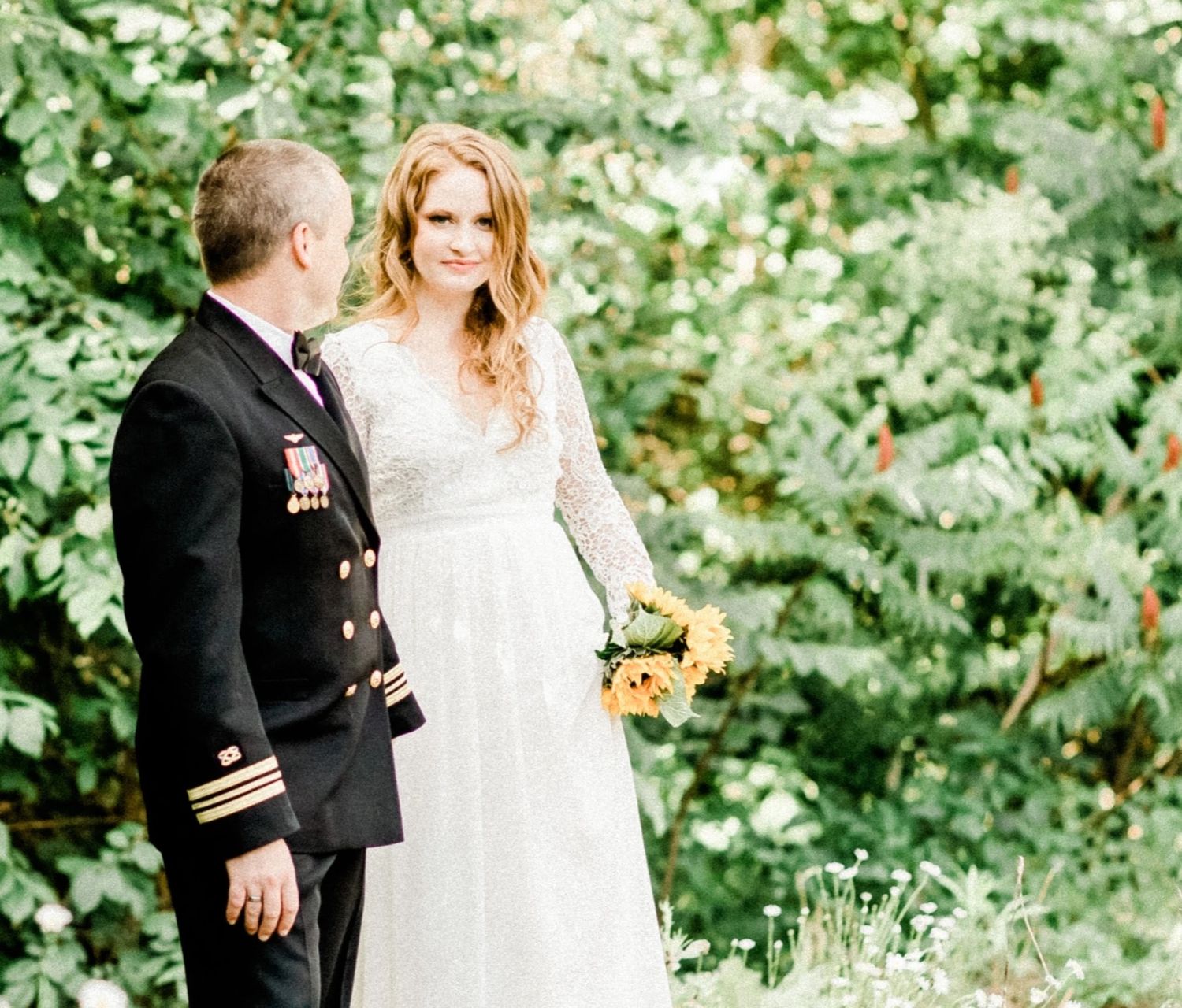 A wedding couple poses together in a lush green garden setting.