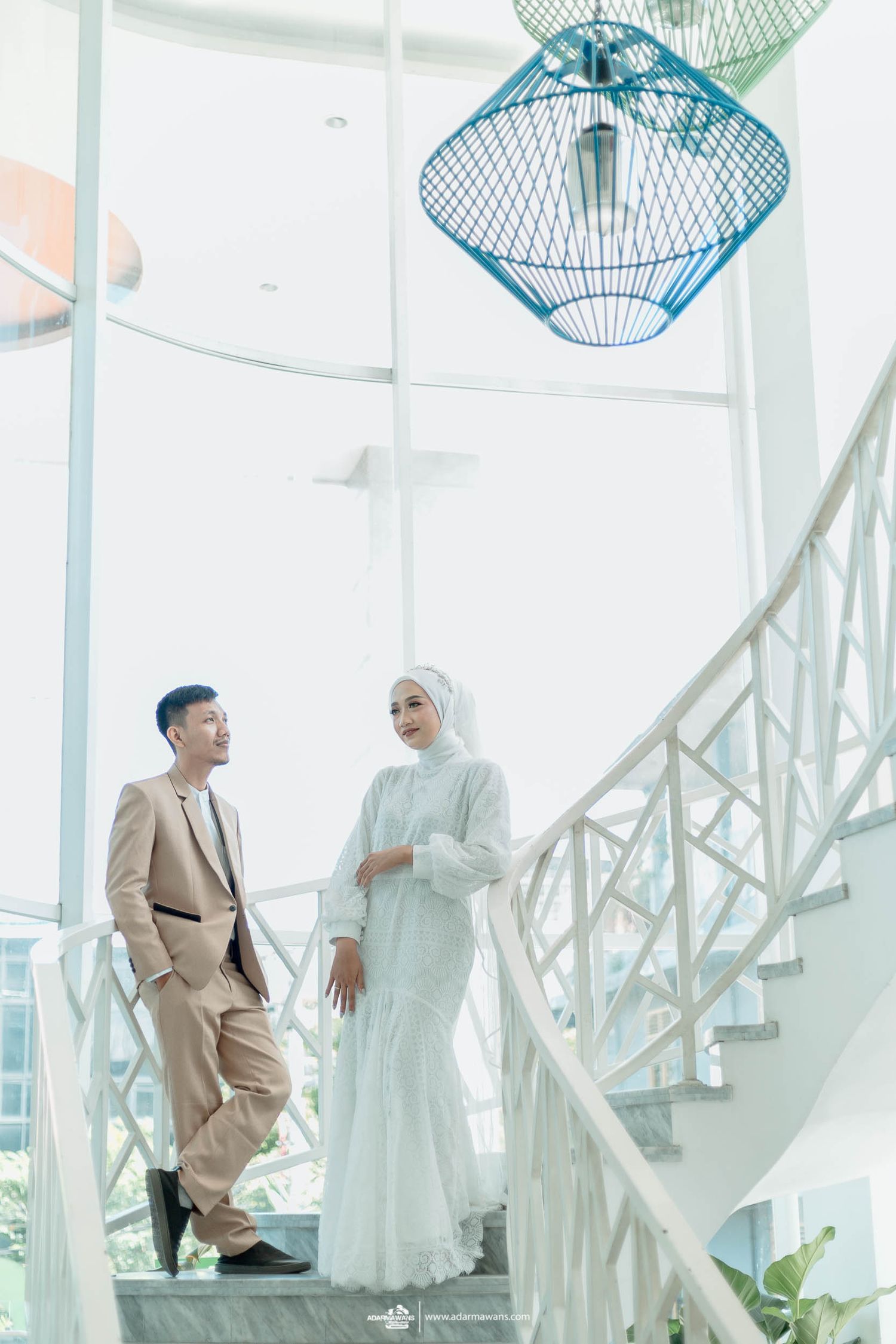 Couple stands on modern staircase with decorative blue pendant lights overhead.
