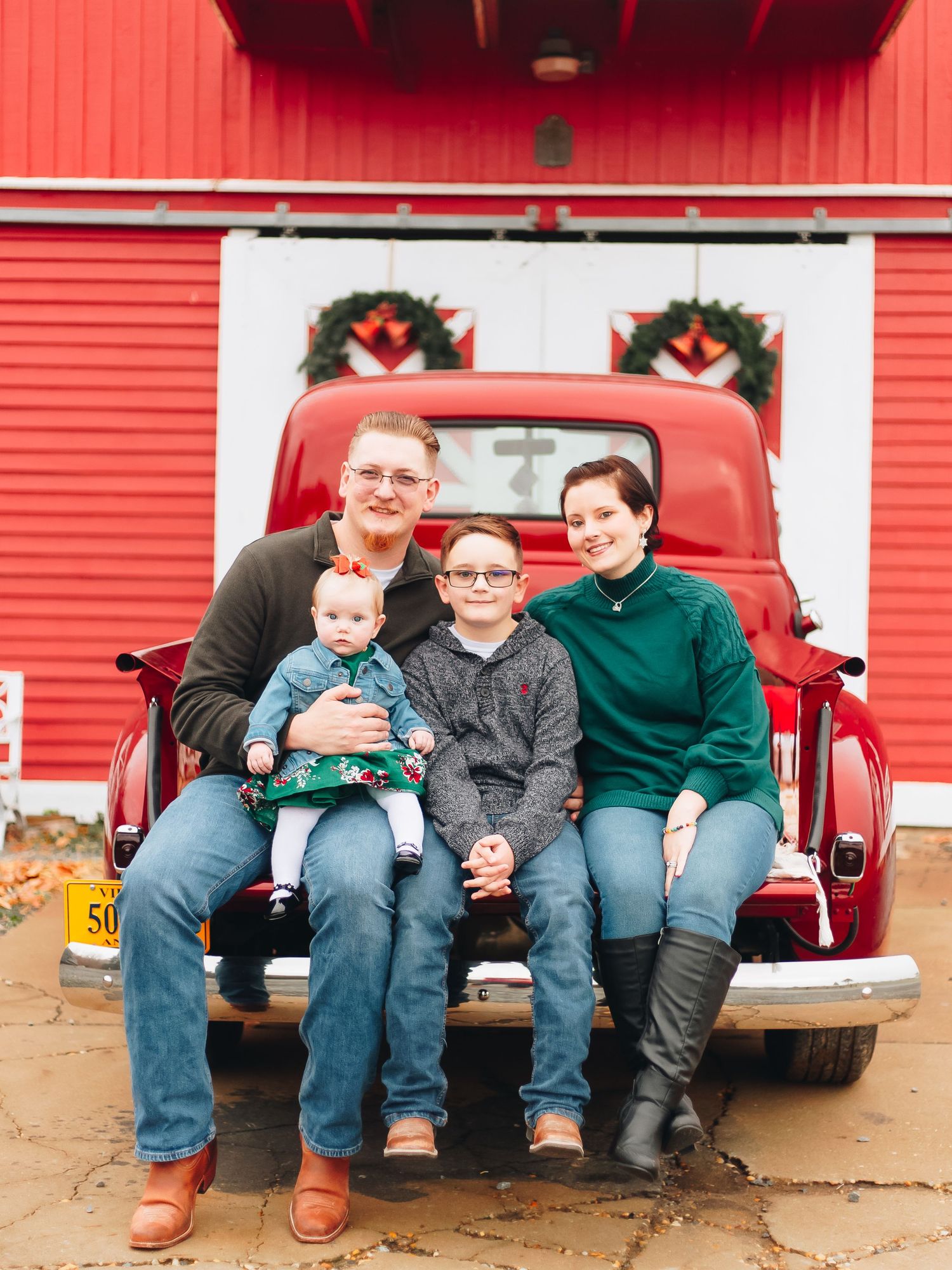 Family sitting together on a red pickup truck tailgate during a casual photo session.