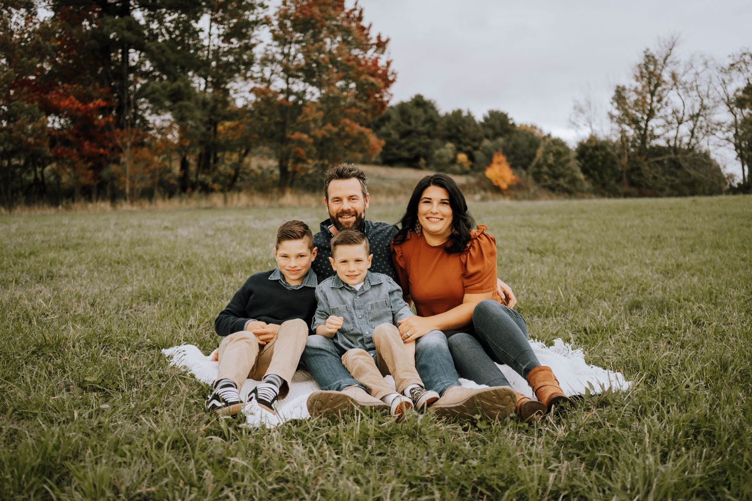 A happy family relaxing together on a blanket in an autumn field during a fall photoshoot.