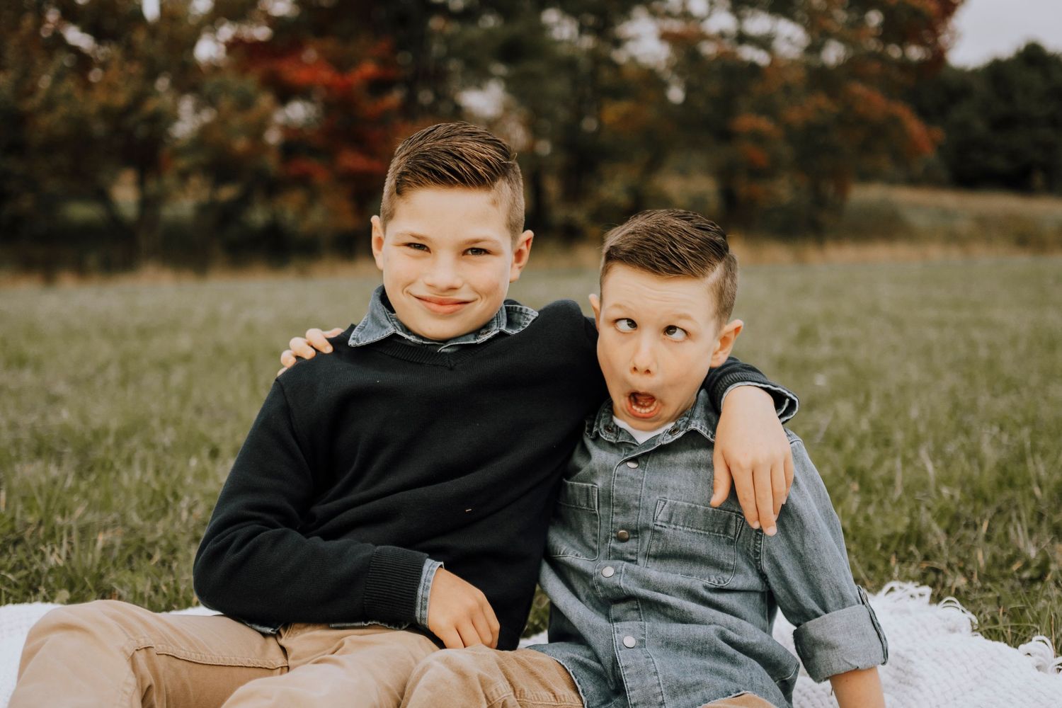 Two playful children sitting together in matching outfits on a blanket outdoors.