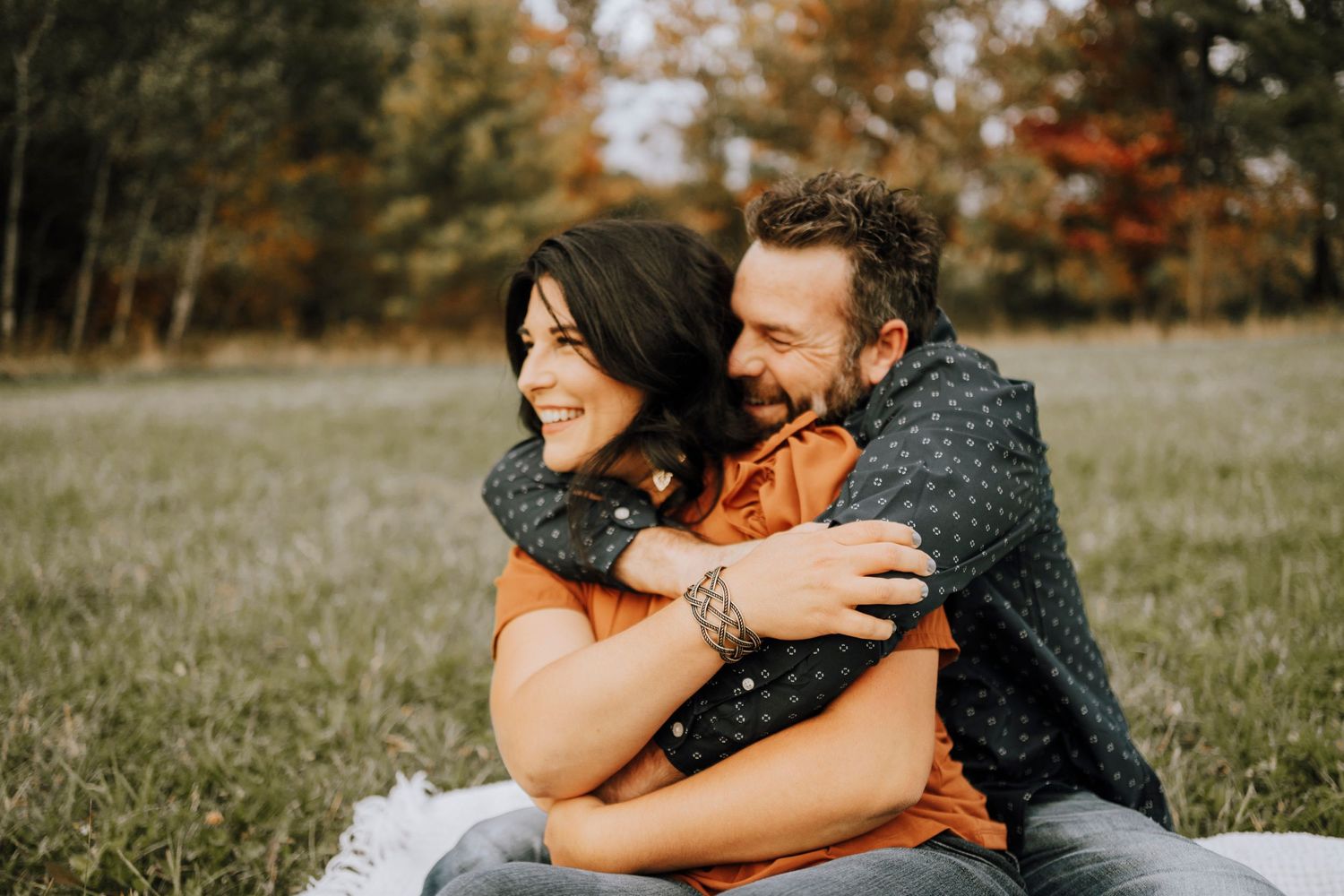 A couple sharing a joyful embrace while sitting on a blanket in an autumn field.