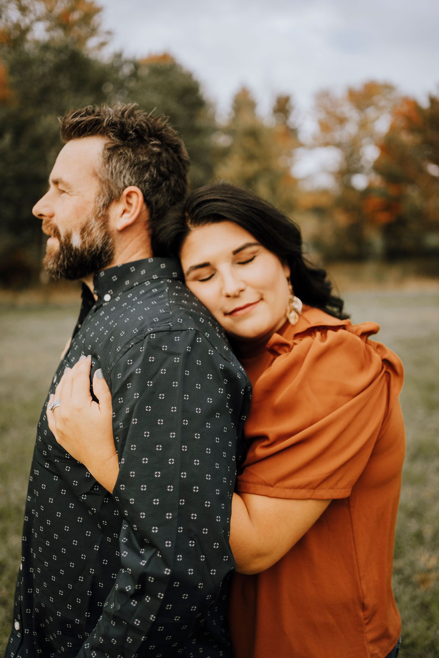 A couple embracing in golden sunlight with fall foliage in the background.