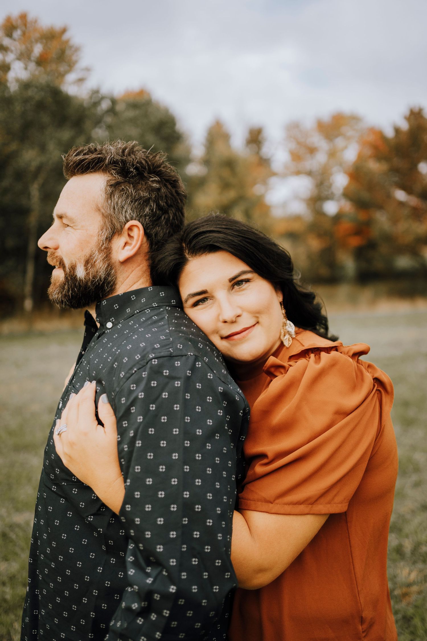 A loving couple poses for a portrait in a field during autumn weather.