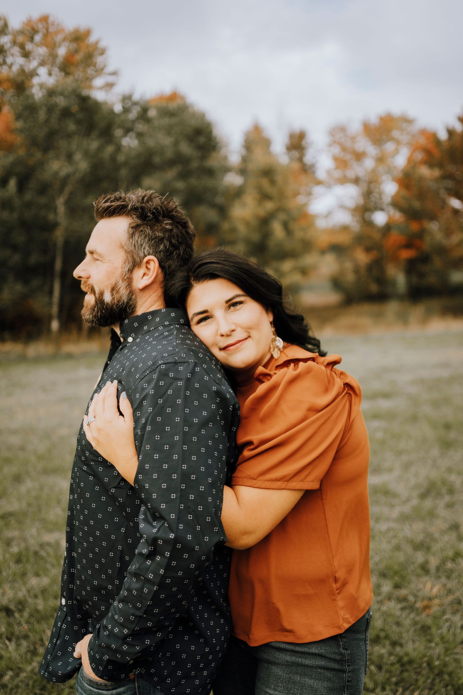 A couple shares an intimate moment while posing in an autumn field.