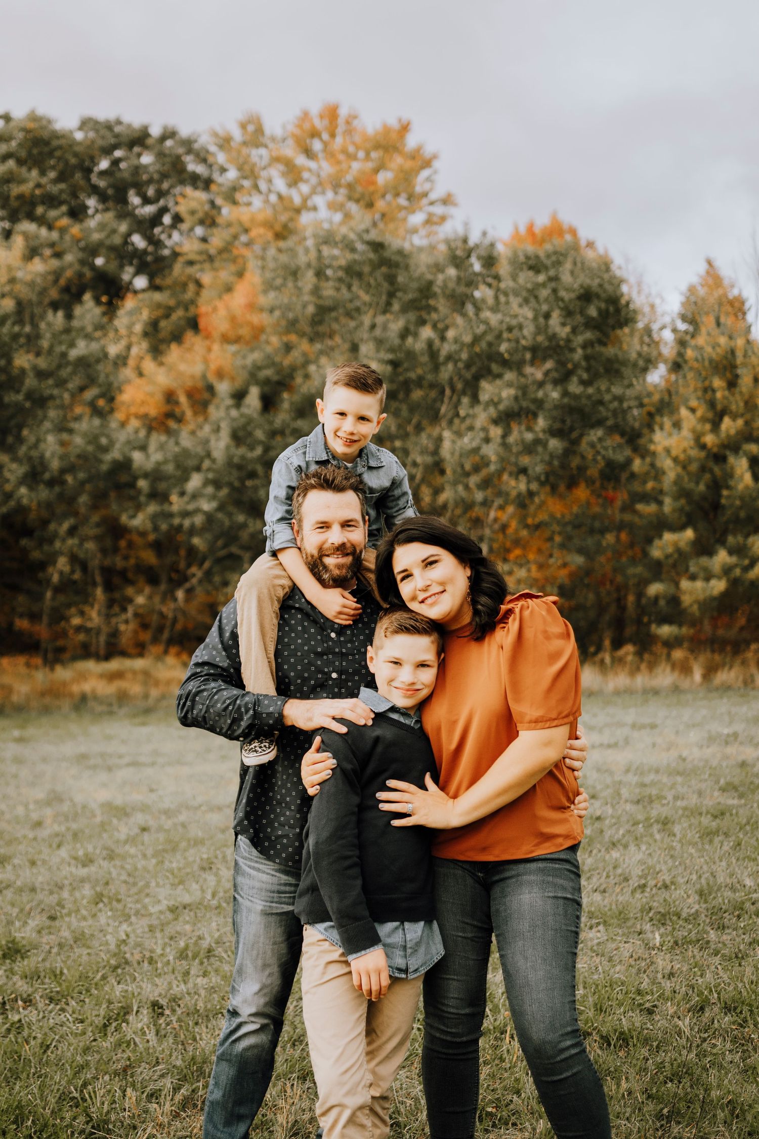 A family of four poses together for a casual outdoor portrait in autumn.