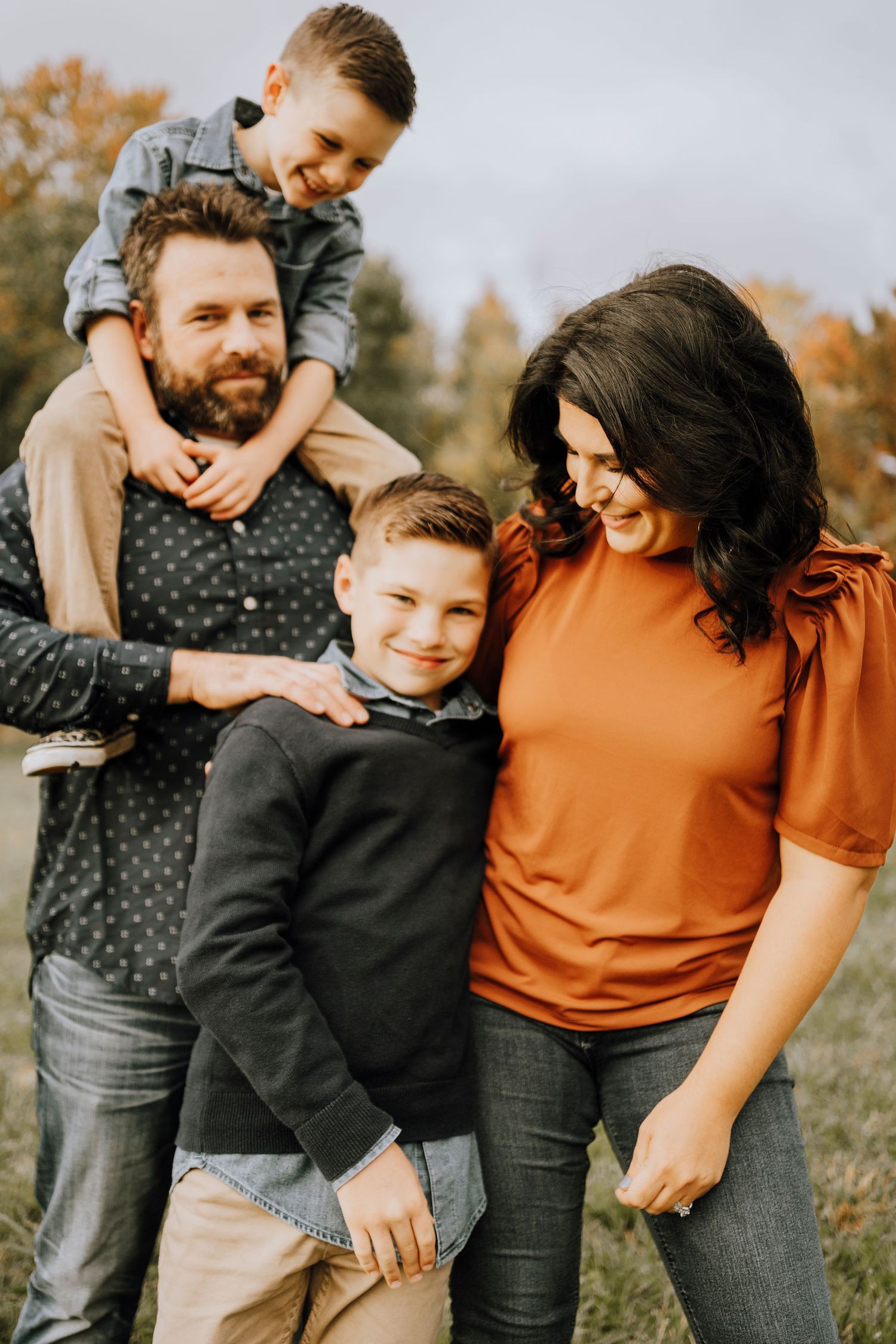 Family embracing and laughing together during autumn outdoor photo session in casual clothing.